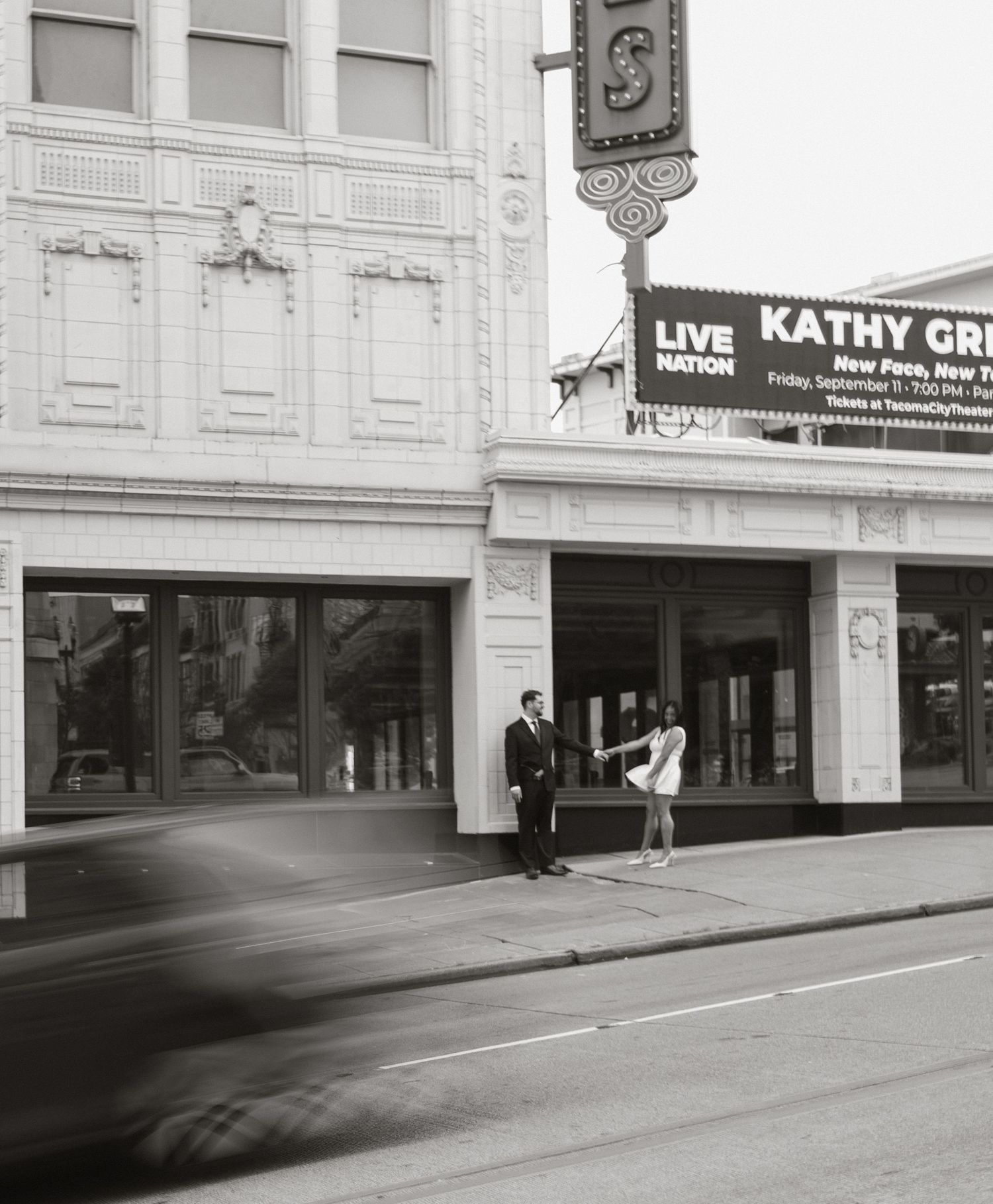 Couple poses outside historic theater in black and white engagement photo.