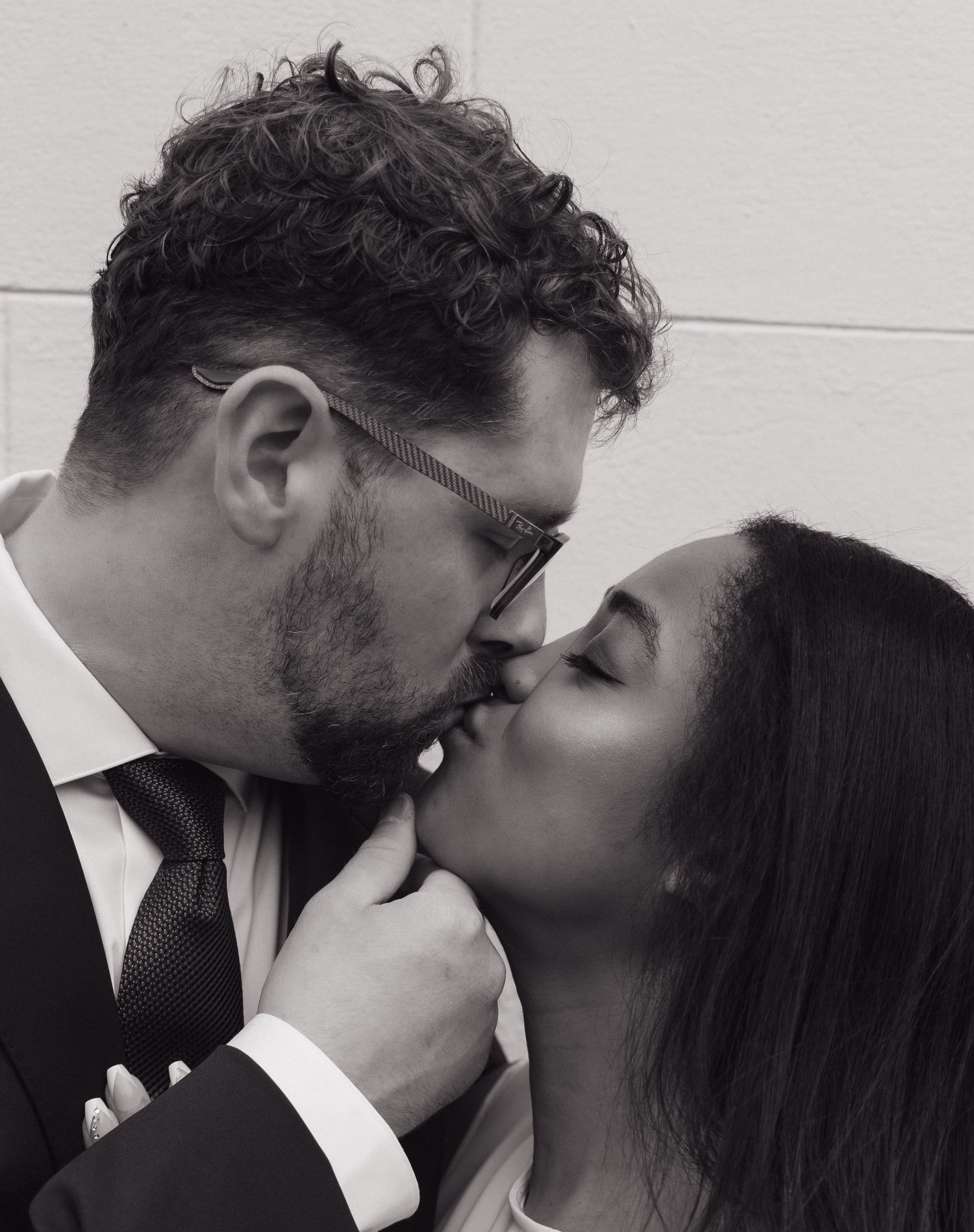 Black and white photo of interracial couple sharing a passionate kiss, groom in suit and tie.