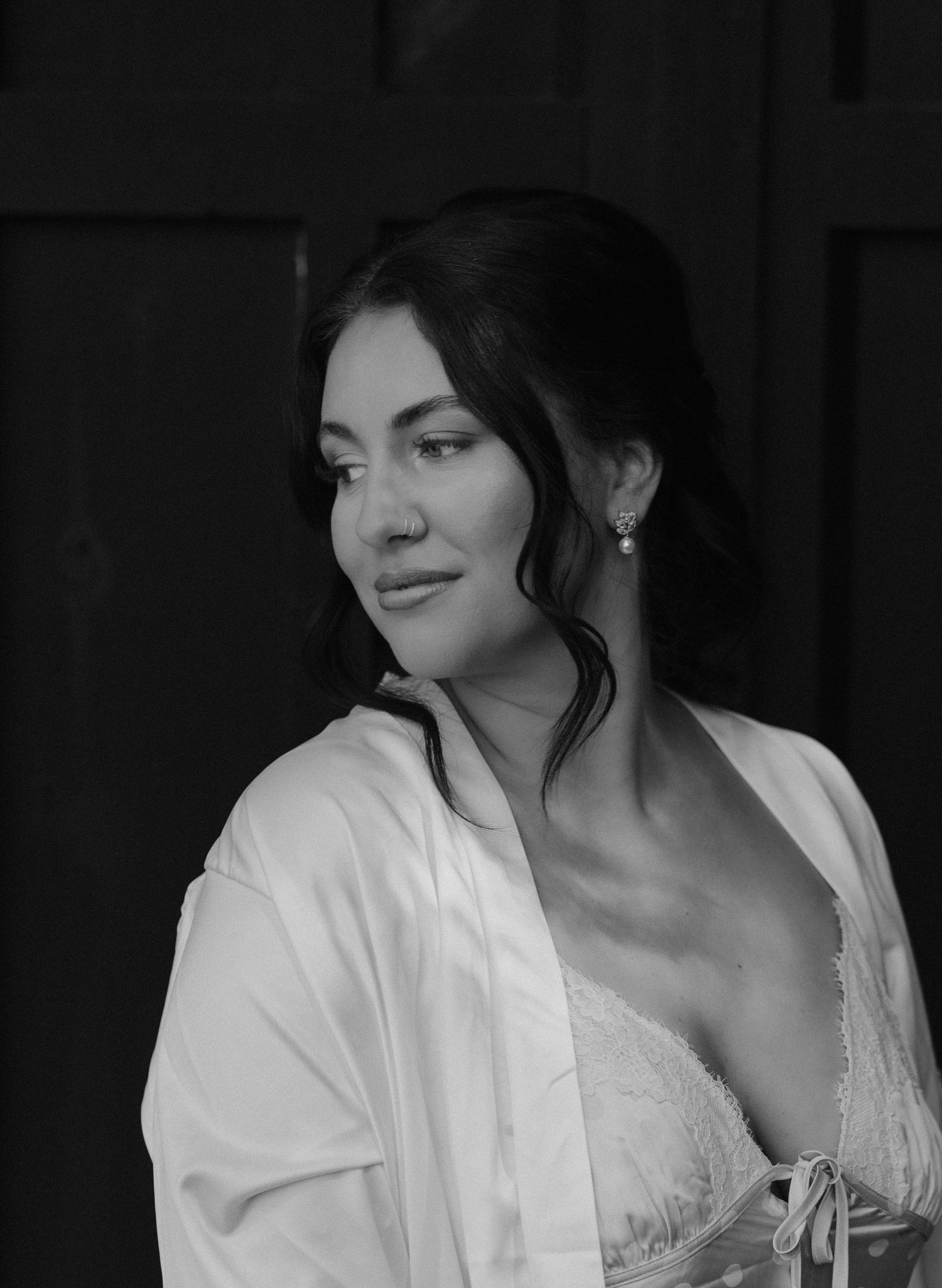 Black and white portrait of a woman in a satin robe with pearl earrings, looking elegantly to the side.