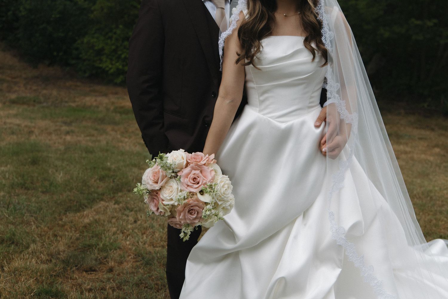Bride in classic white ball gown holding blush and white rose bouquet with groom outdoors.