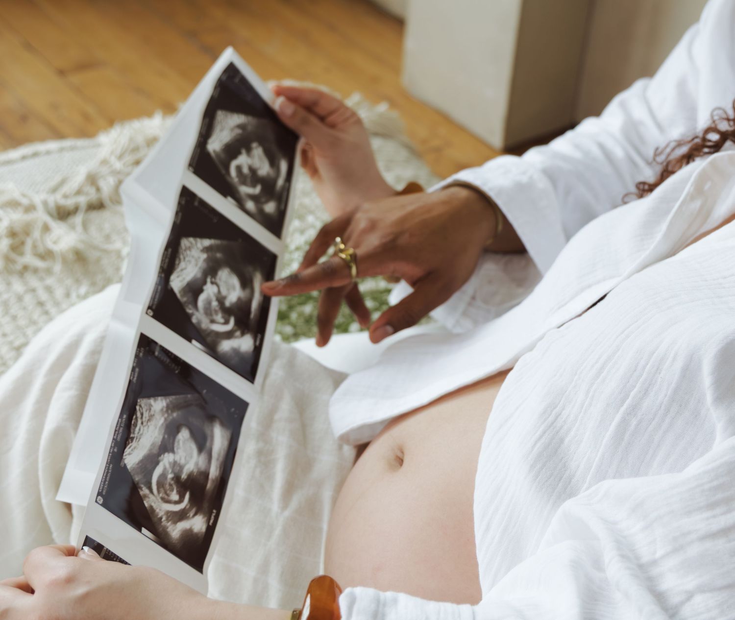 Pregnant woman in white shirt reviewing ultrasound photos while resting with visible baby bump.