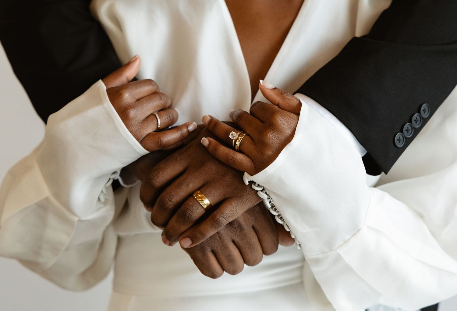 Close-up of newlywed couple's hands clasped together showing gold wedding rings and bracelets.