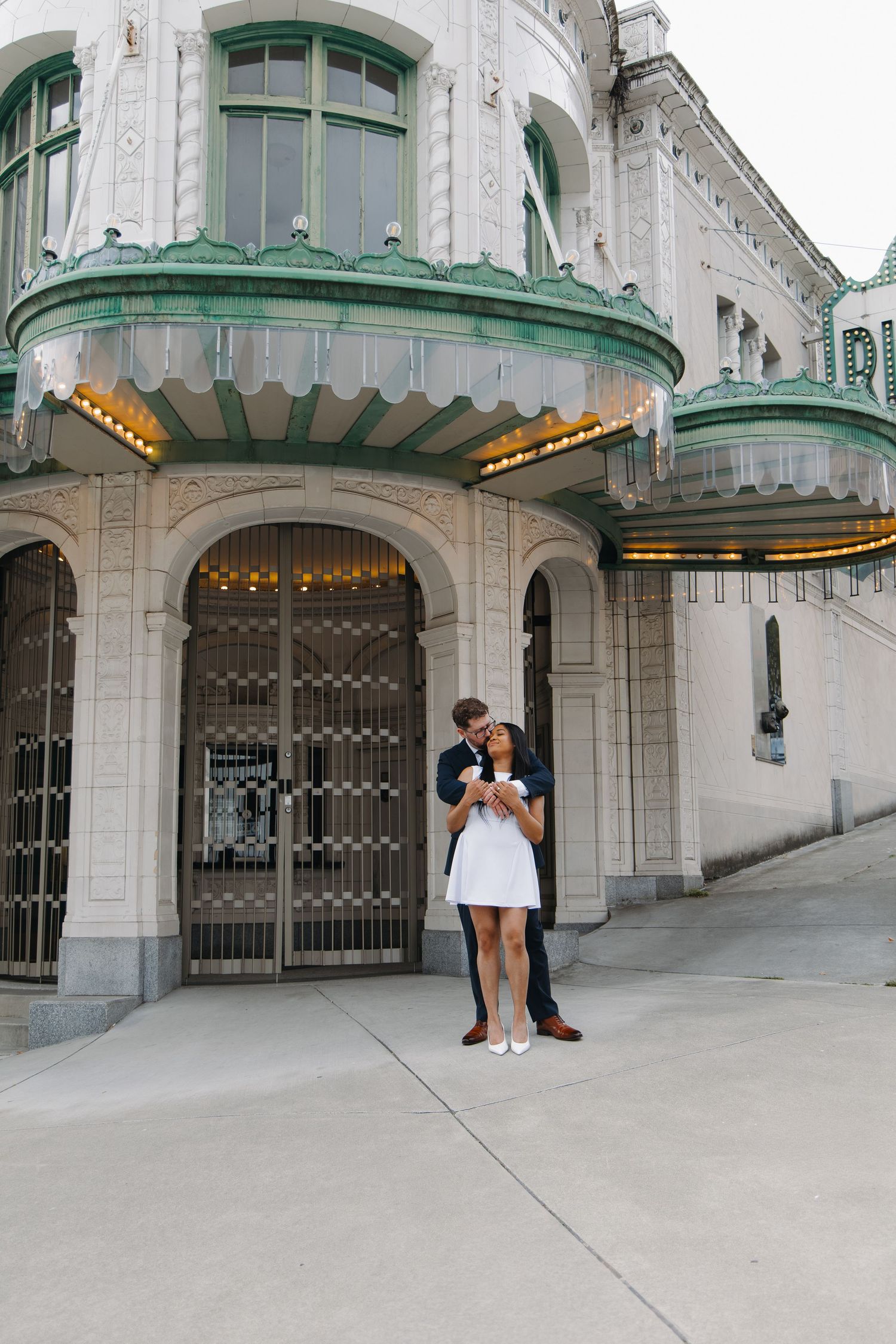 Couple embracing and kissing outside ornate historic building with green copper architectural details.