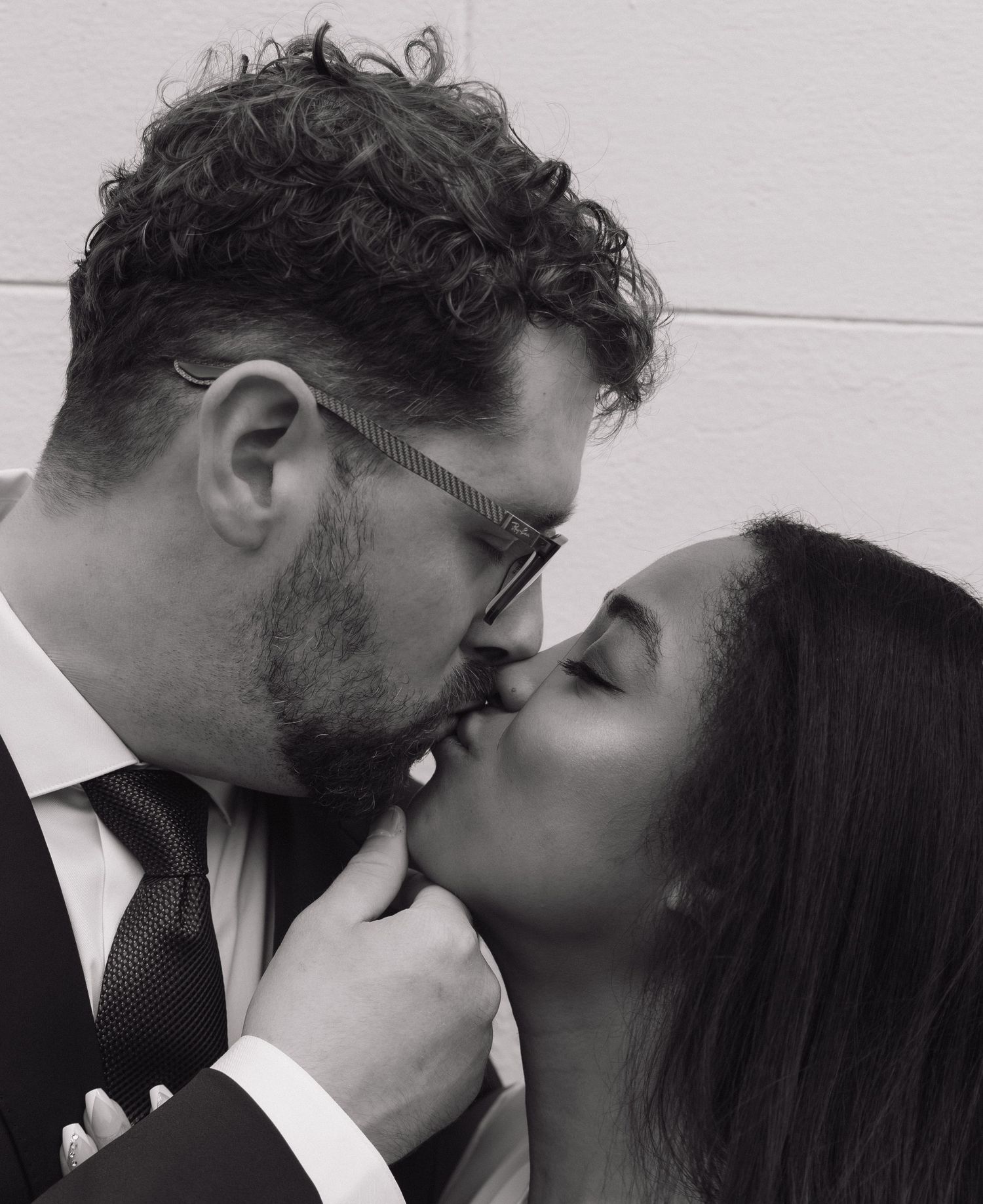 Black and white photo of a couple sharing a passionate kiss in formal wedding attire.