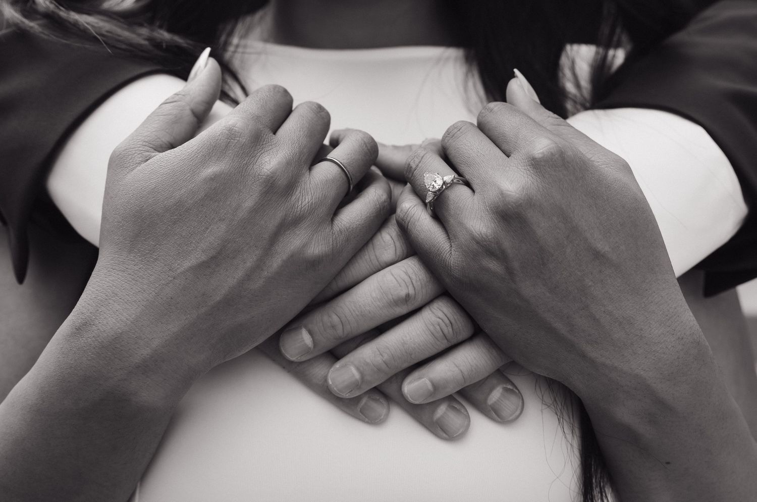 Black and white close-up of couple's hands clasped together showing engagement ring.