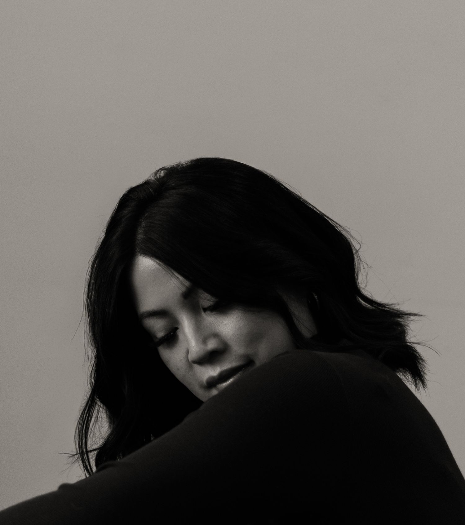 Black and white portrait of woman with dark hair looking down in contemplative pose.