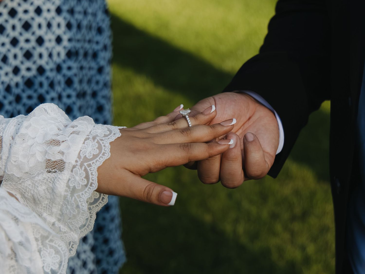 Close-up of couple holding hands during ring exchange at outdoor wedding ceremony.