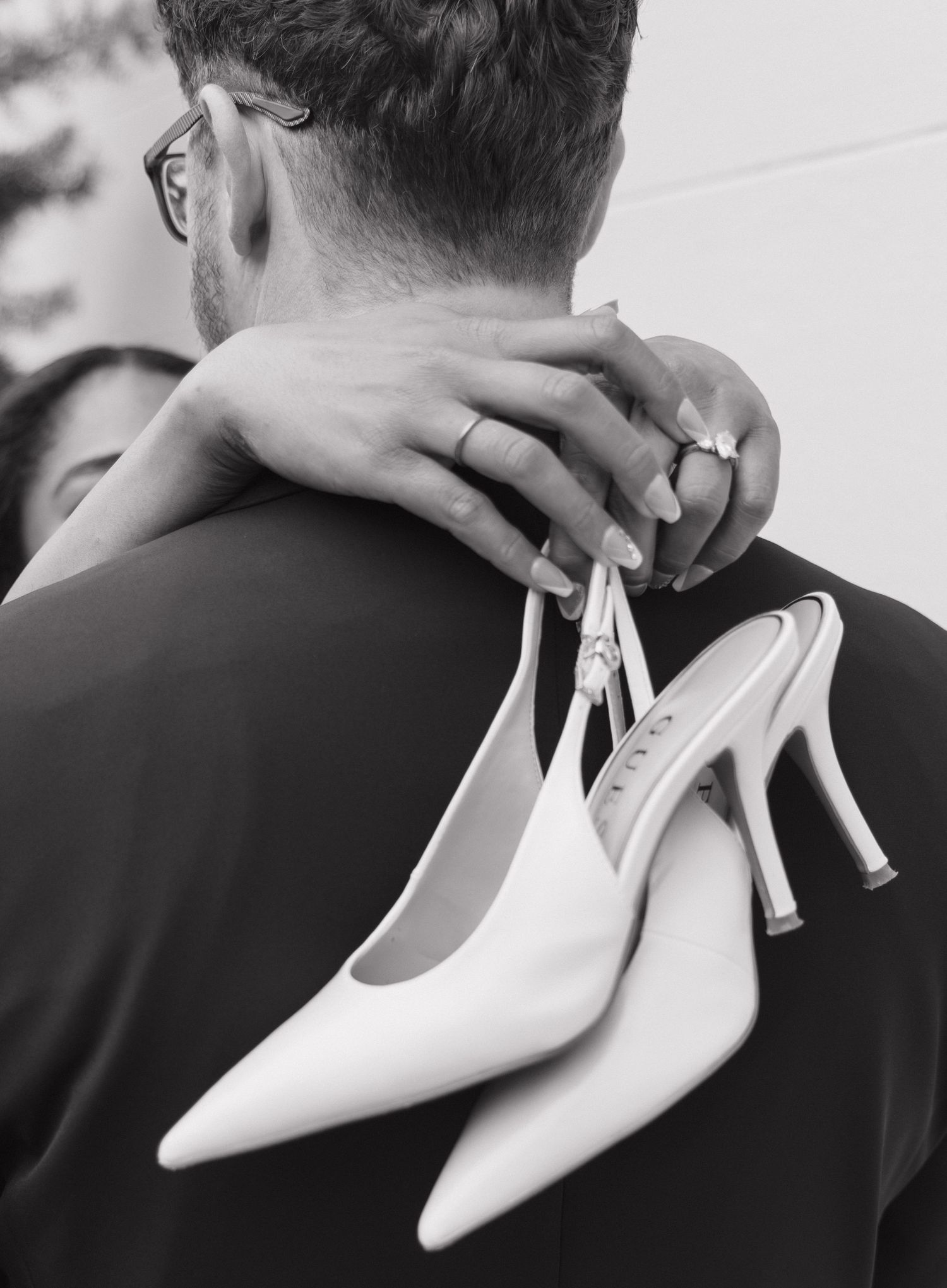 Black and white close-up of bride holding heels while embracing groom.