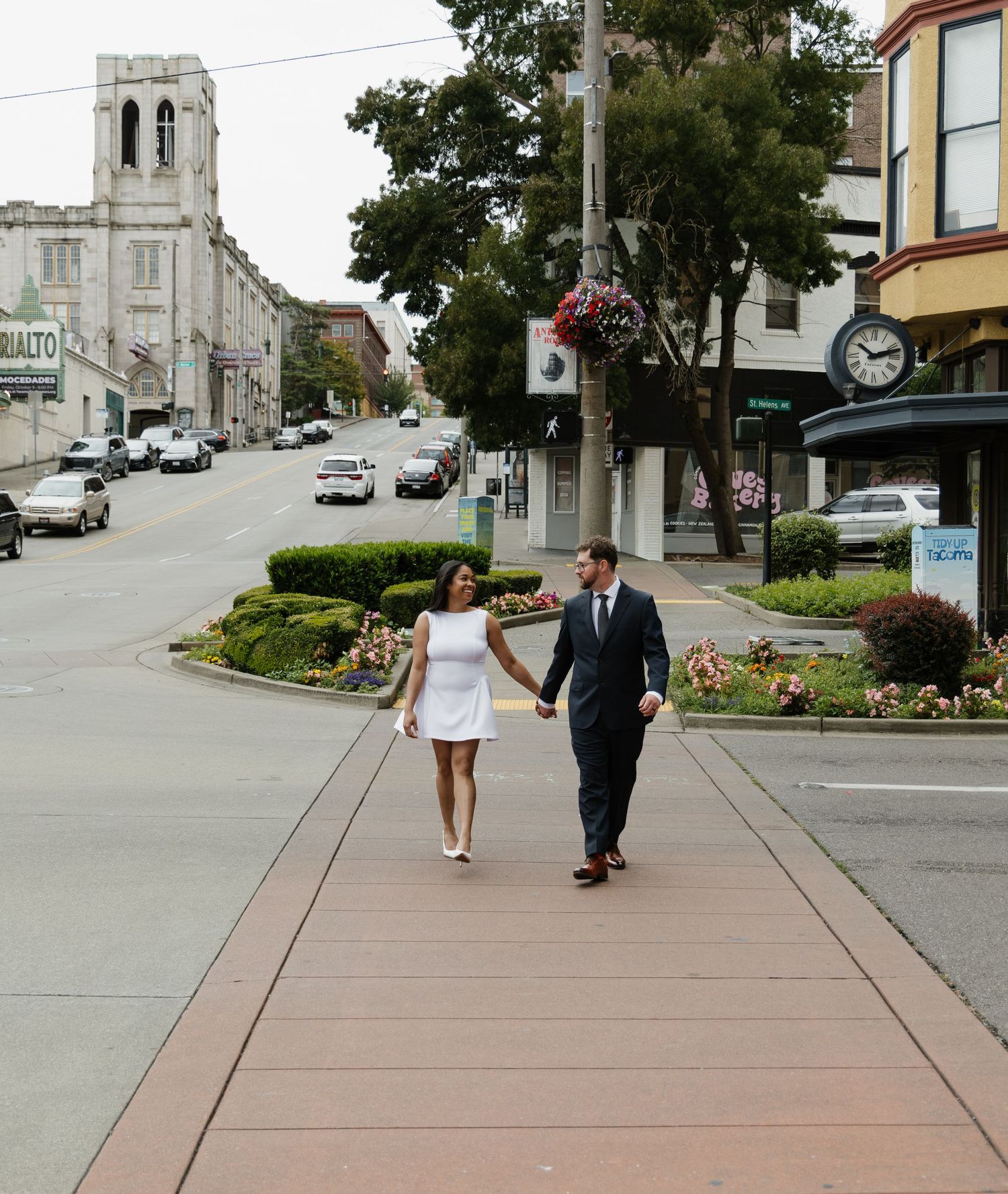 Newlyweds walk hand in hand along charming small town sidewalk in wedding attire.