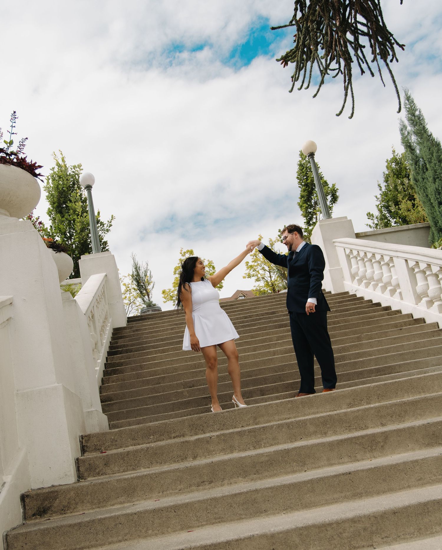 Couple dancing on grand outdoor staircase, woman in white dress and man in dark suit.