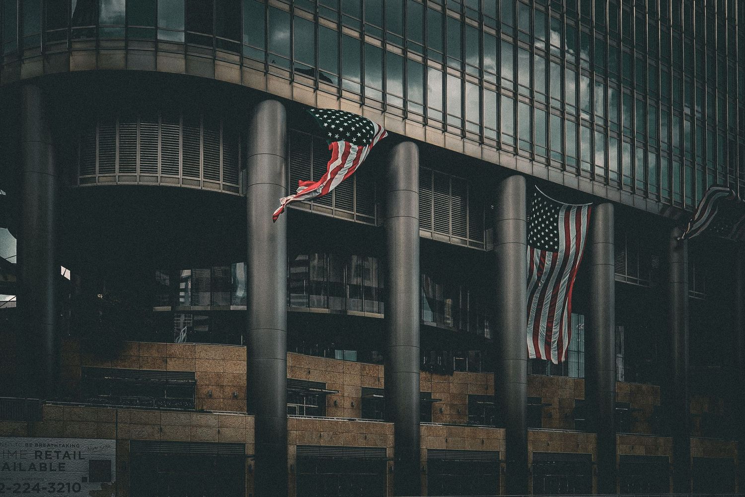 American flags hang on columns of a dark modern building facade in moody urban architectural photography.