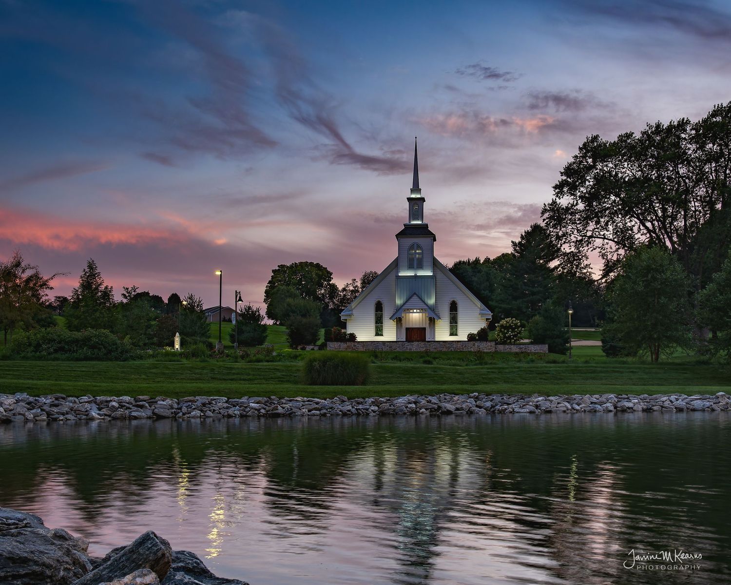 White New England church with steeple reflected in calm pond at colorful sunset dusk. Willow Valley, Lancaster Pa