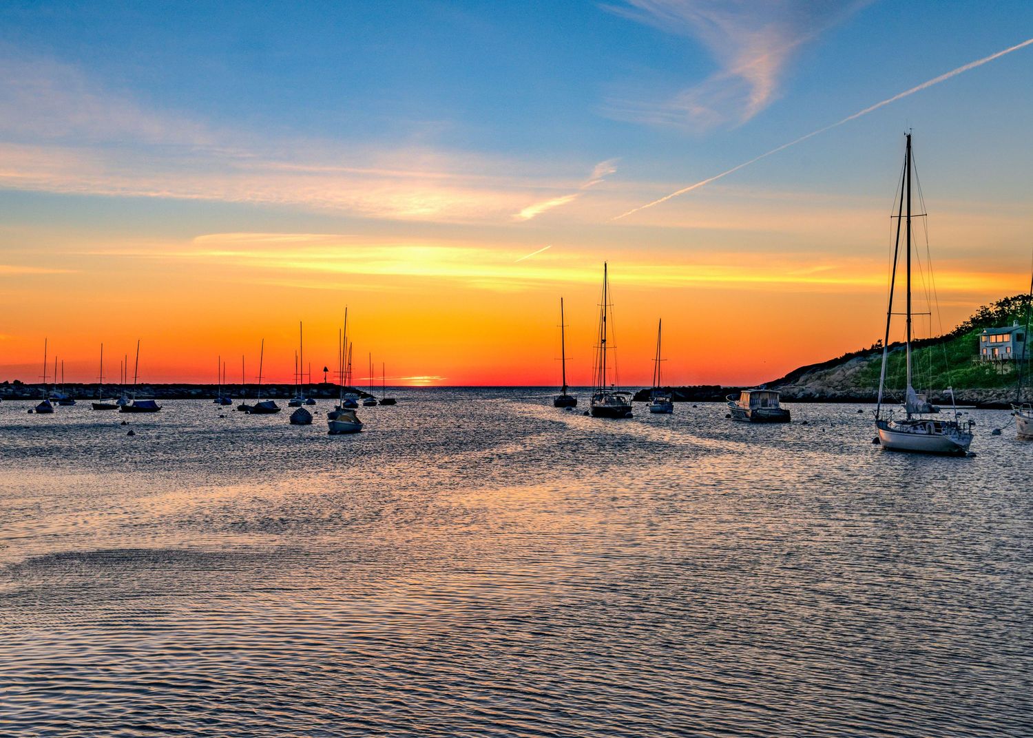 Sunrise from Rockport Massachusett's T Wharf with sailboats in a calm harbor at with vibrant orange and blue skies reflecting on the water.