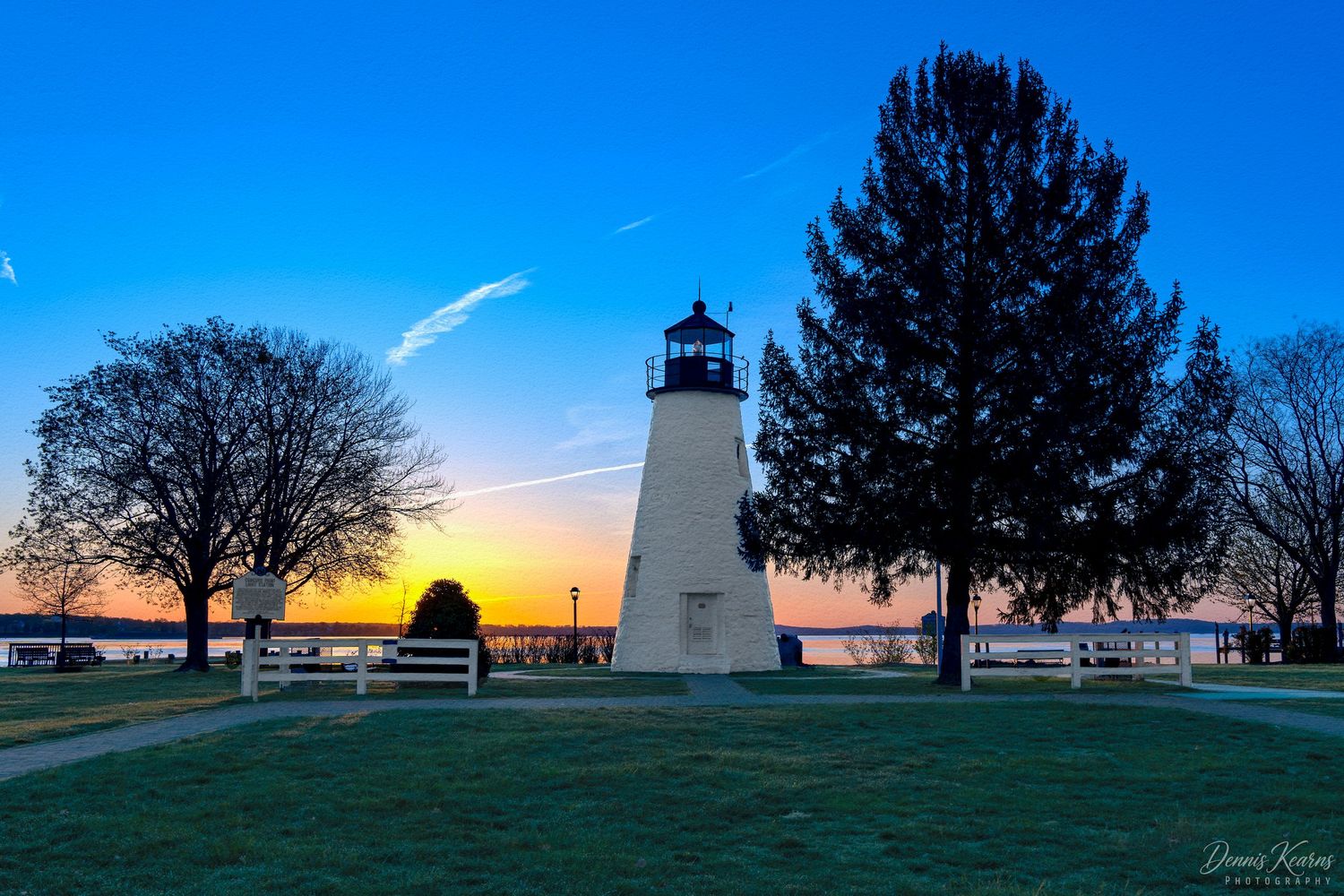 Concord Point Lighthouse at sunset with colorful sky, surrounded by trees near the Chesapeake Bay waterfront.