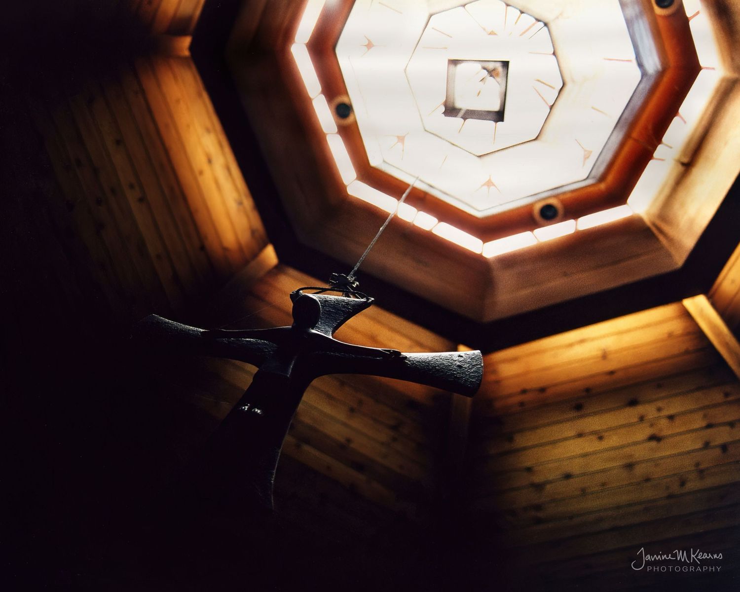 Wrought iron crucifix in the chapel at Camaldoli Hermitage, Big Sur, California. Warm wooden octagonal ceiling surrounding skylight.