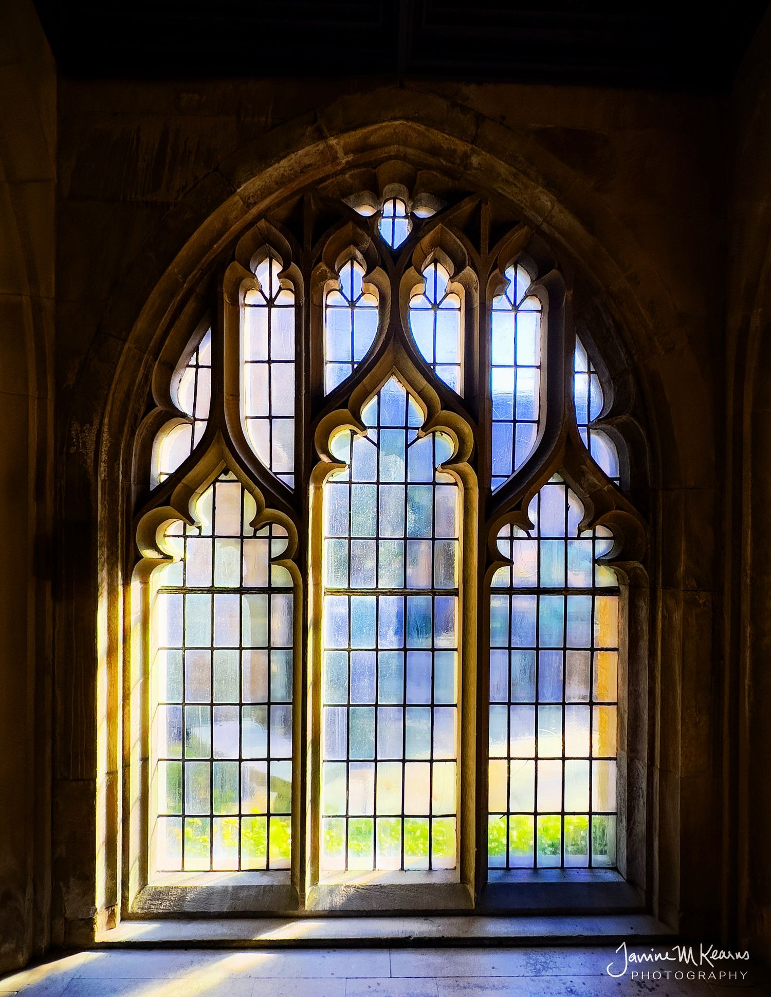 Gothic arched stained glass window in a stone church, with warm golden light filtering through colorful leaded panes.
