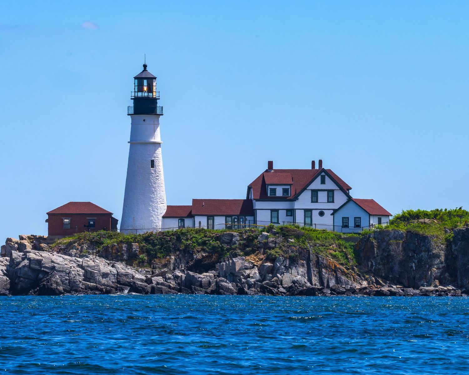 Iconic Portland Head Light lighthouse with red-roofed keeper's house on rugged rocky Maine coastline in summer.