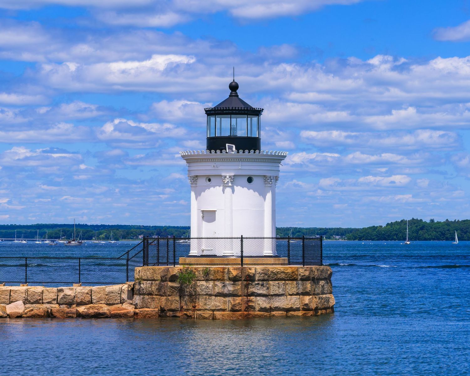 Portland Breakwater Bug Light white lighthouse on stone pier surrounded by blue harbor waters in South Portland, Maine.