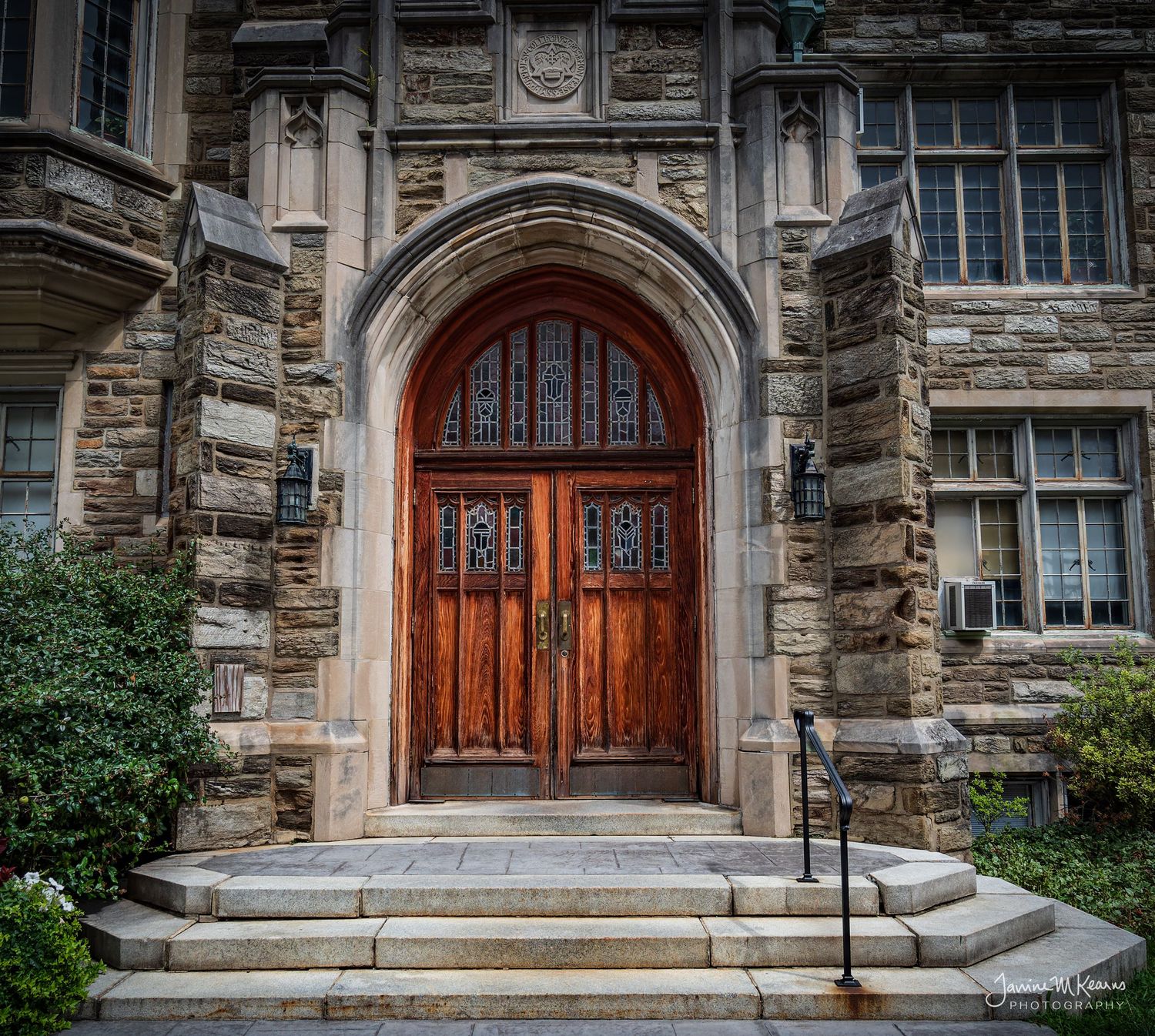Gothic stone building entrance with ornate wooden arched double doors, decorative ironwork, and stone steps.
