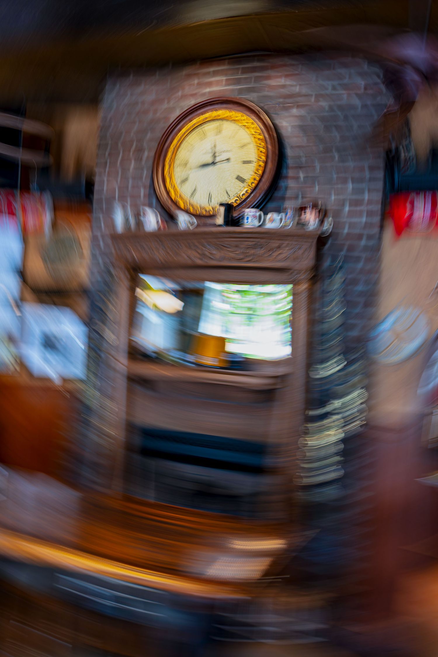 Blurred vintage clock on brick fireplace mantel with mirror and decorative items in a cozy rustic interior.