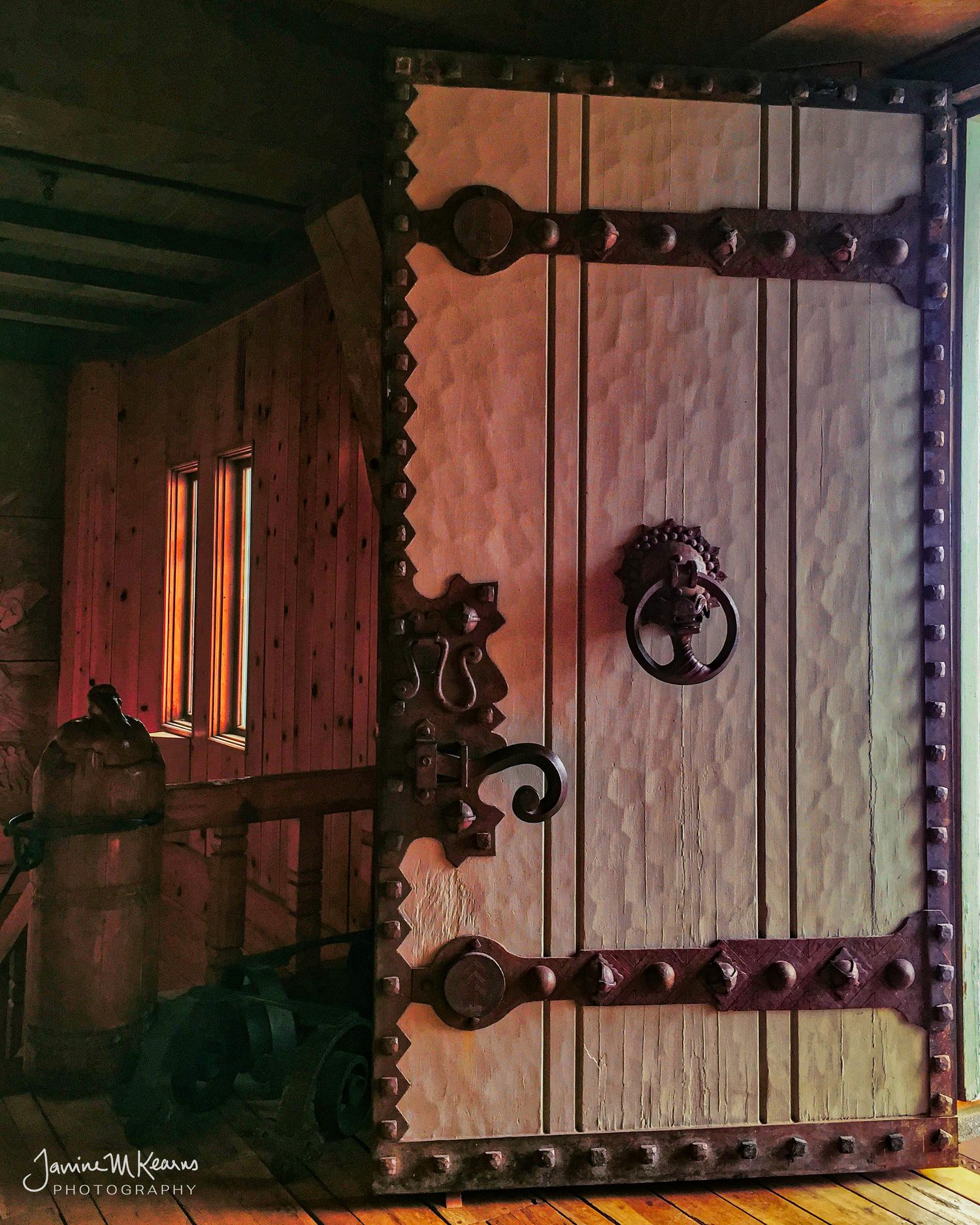 Ornate medieval wooden door with decorative iron hardware, studded border, and lion knocker in rustic interior setting.