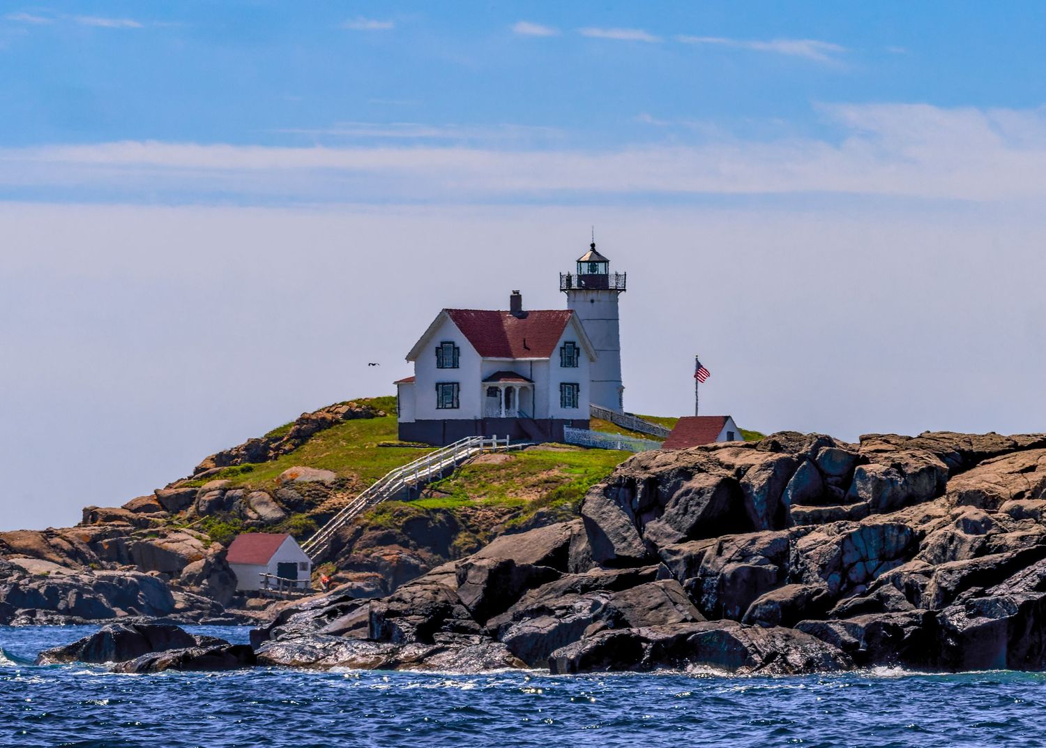 Cape Neddick Nubble Lighthouse with red-roofed keeper's house on rocky island surrounded by blue ocean in York, Maine.