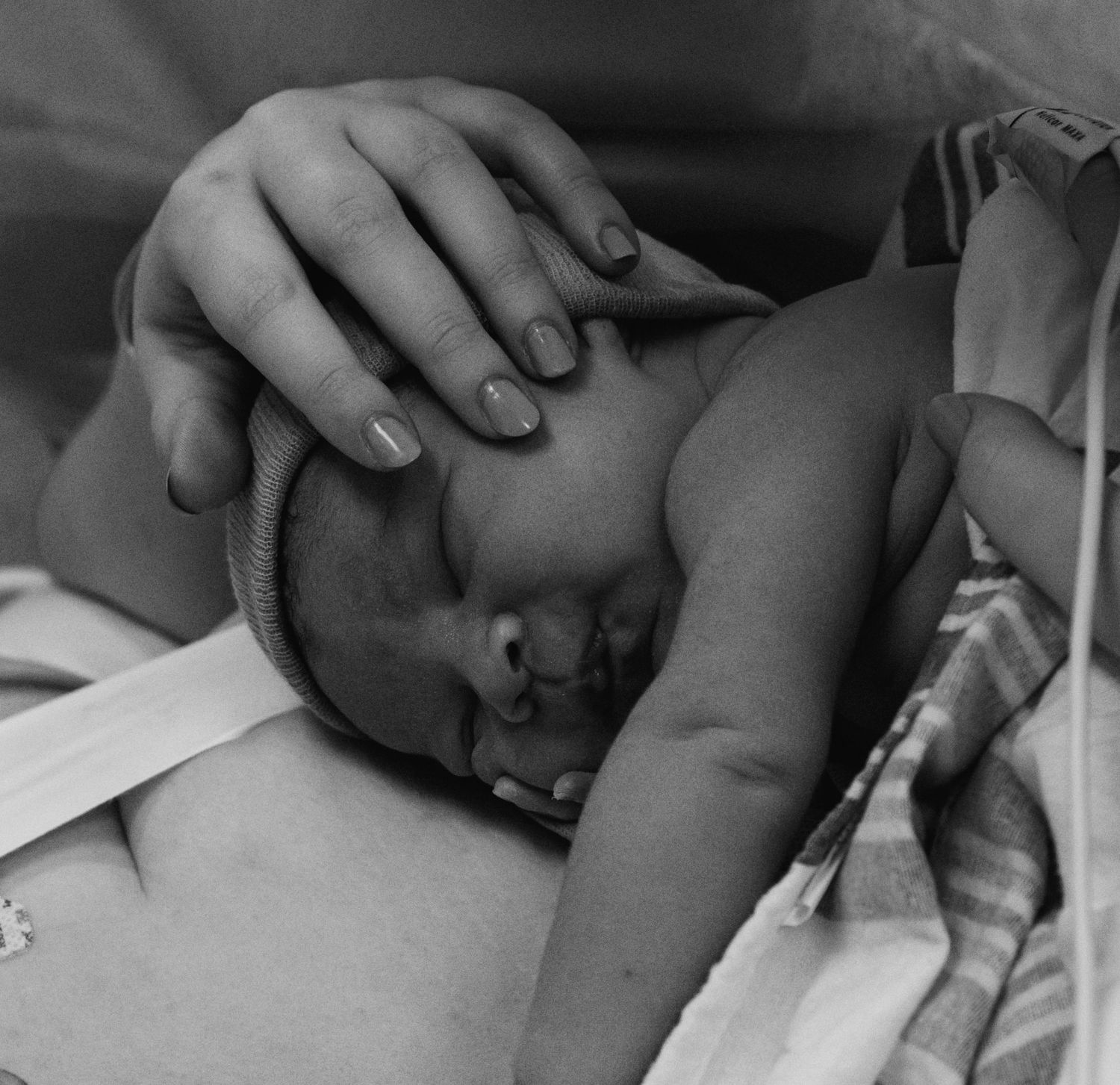 Black and white image of a parent's hand gently cradling a sleeping newborn baby in hospital.
