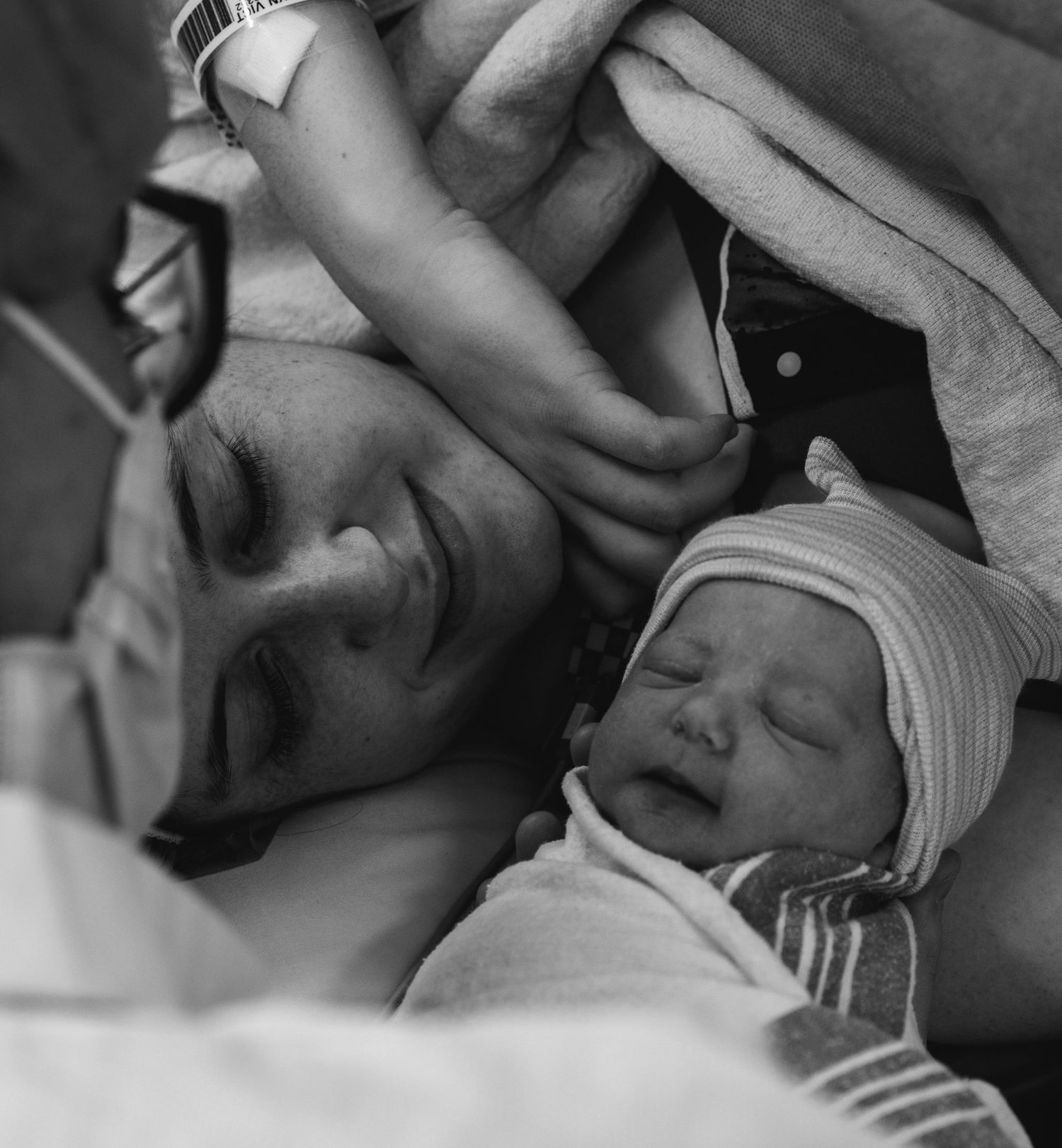 Black and white photo of exhausted new mother lying in hospital bed with sleeping newborn baby after childbirth.