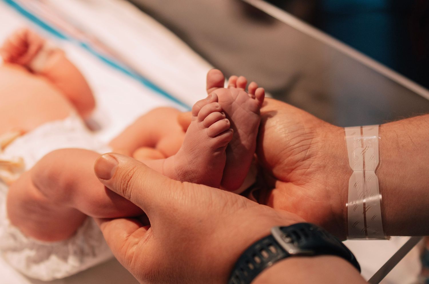 Parent's hands tenderly holding tiny newborn baby feet in a hospital setting.