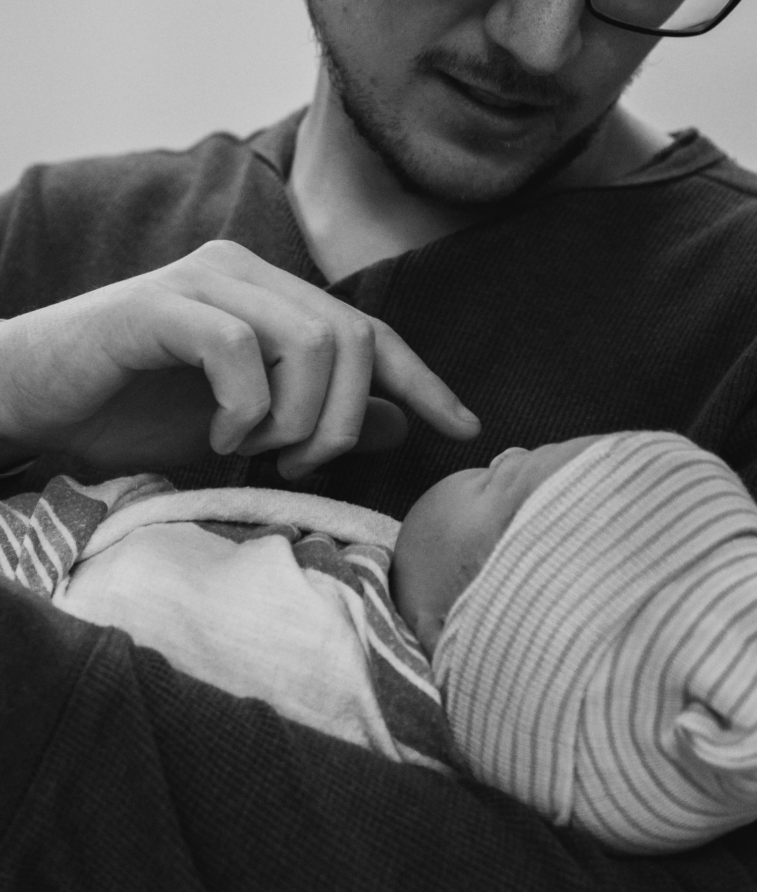 Black and white photo of a father cradling his newborn baby while pointing at the infant.