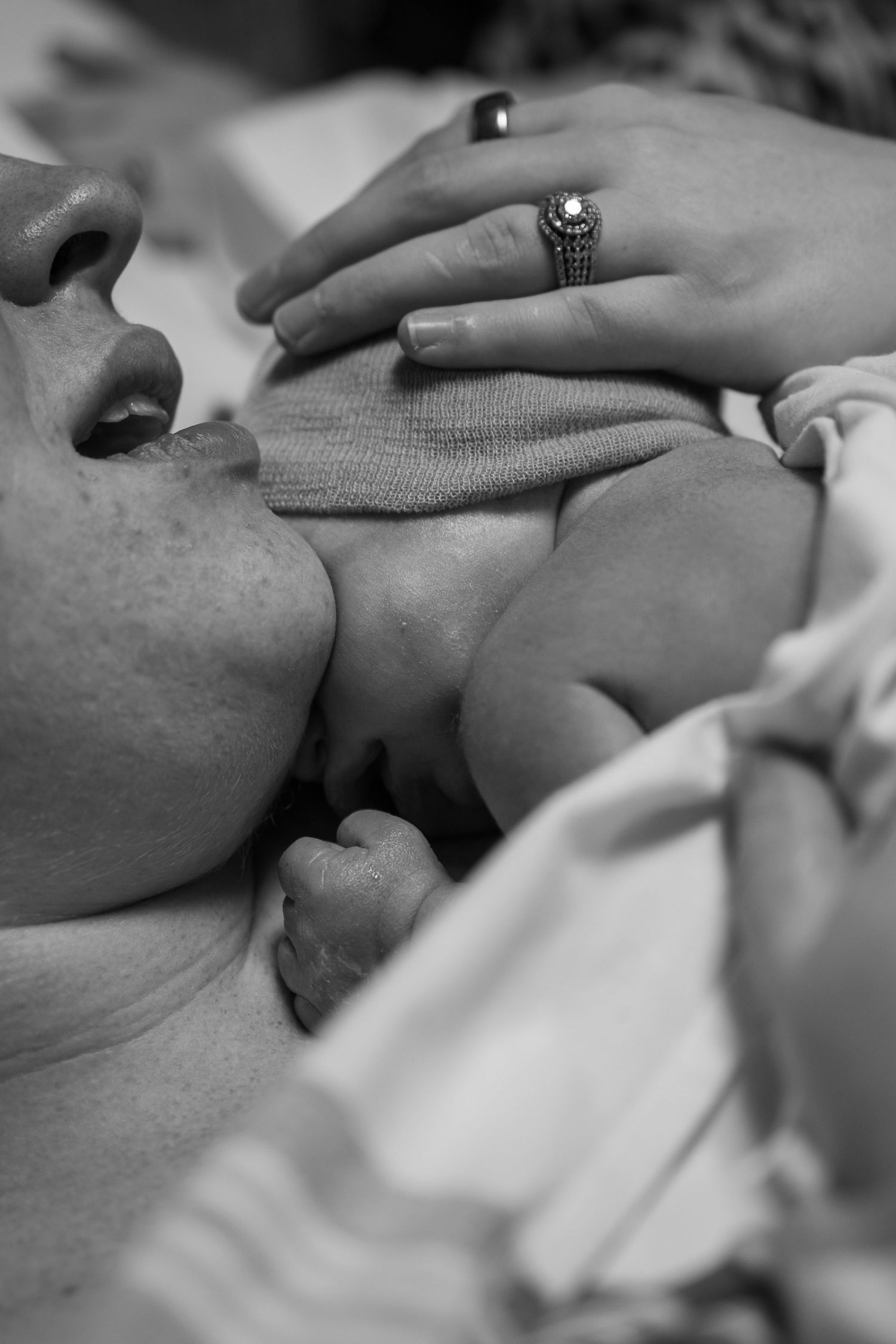 Black and white photo of parent kissing newborn baby while wearing a diamond engagement ring.