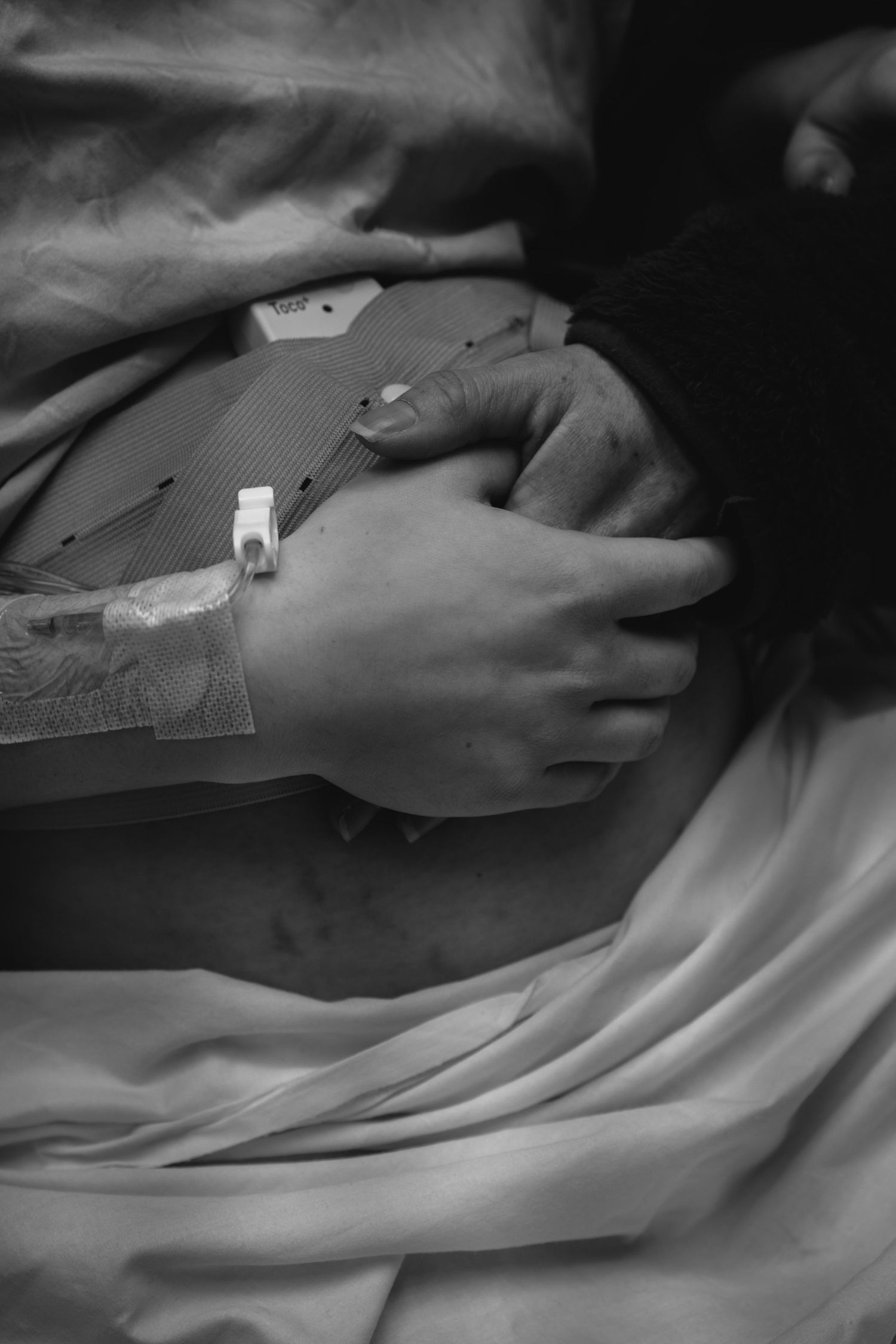 Close-up black and white photo of new mother's hand with hospital ID bracelet and IV after giving birth.