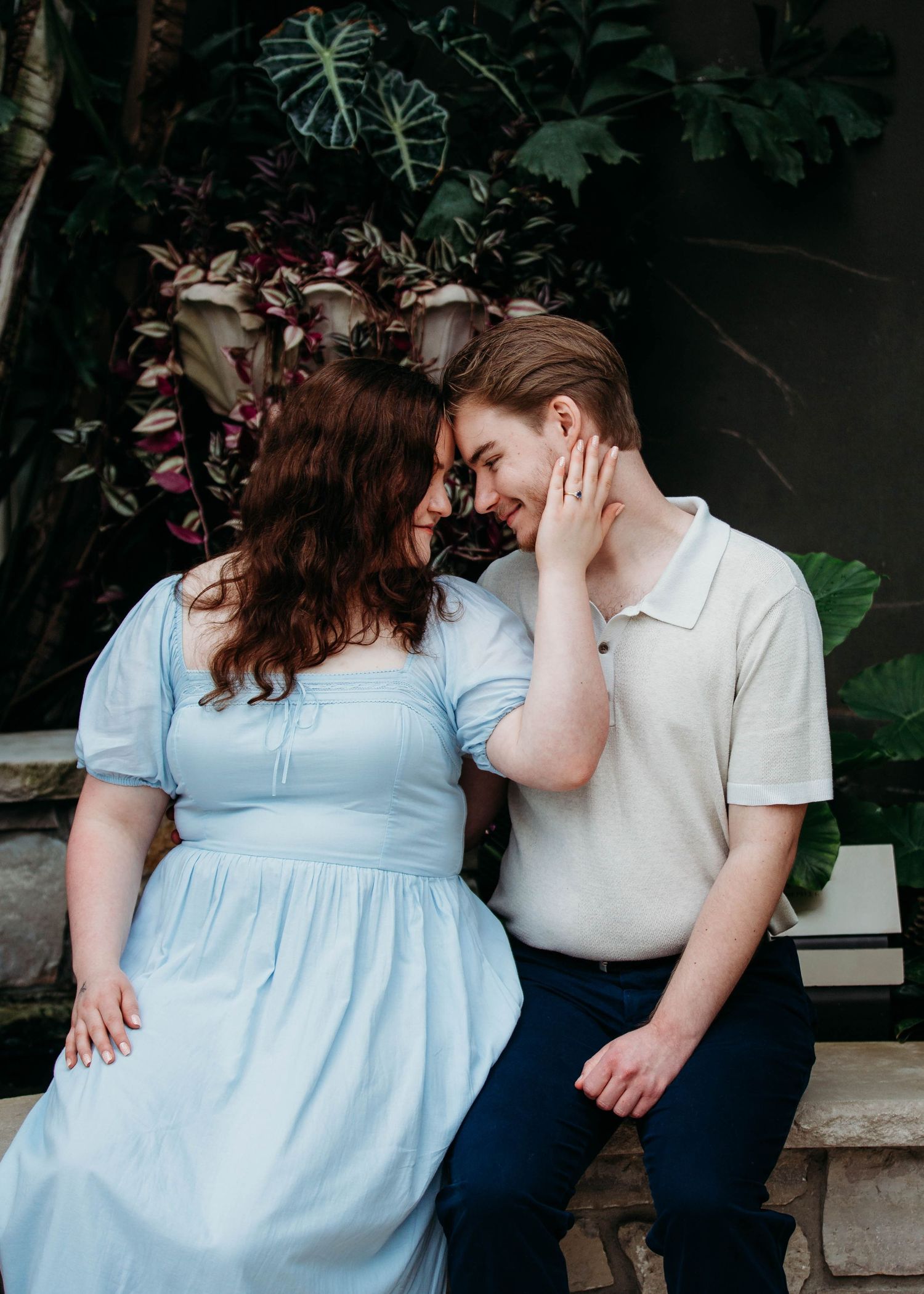 Couple touching foreheads romantically, woman in light blue dress with engagement ring visible.