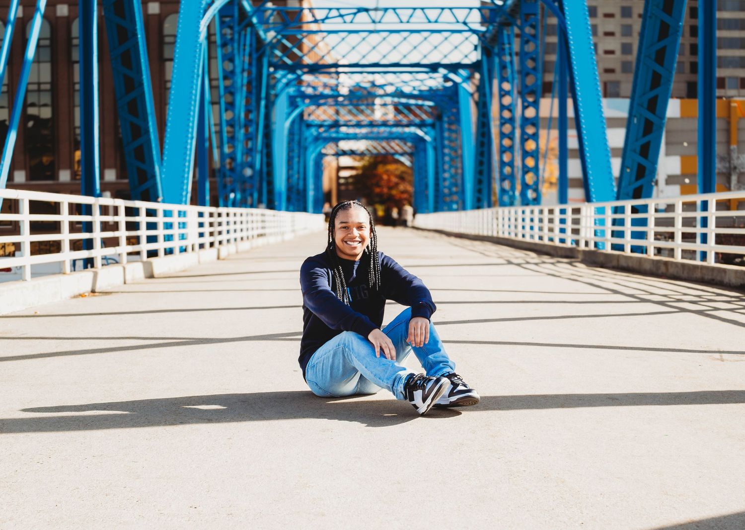 Teen girl sitting on blue bridge deck in casual outfit.