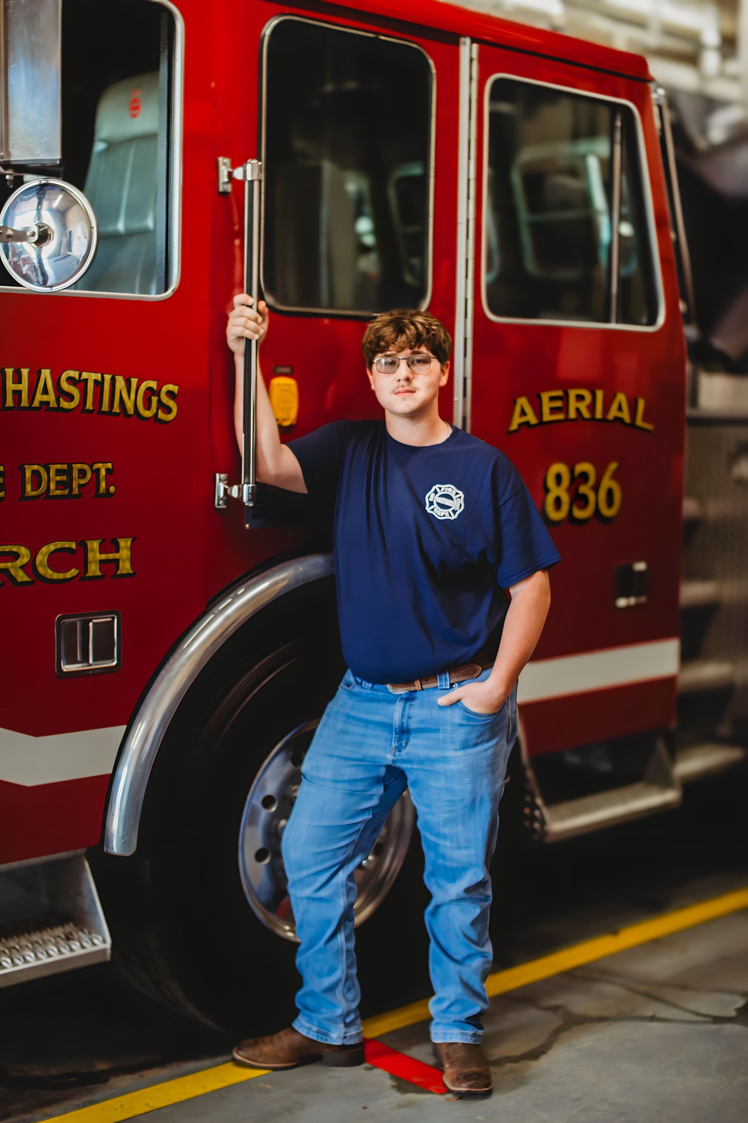 Teen boy in navy shirt poses beside a red Hastings Fire Department aerial truck 836.