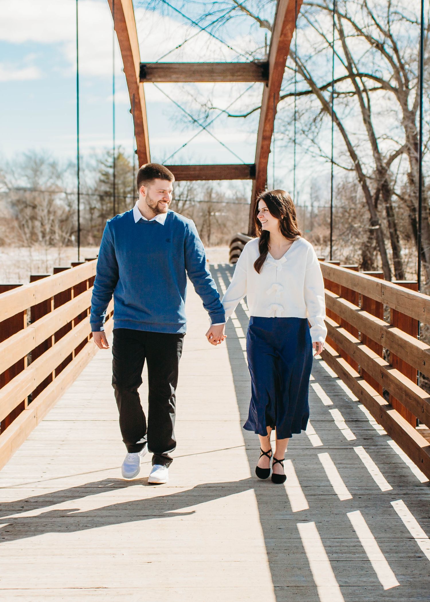 Couple holding hands and walking on a wooden bridge on a sunny winter day.