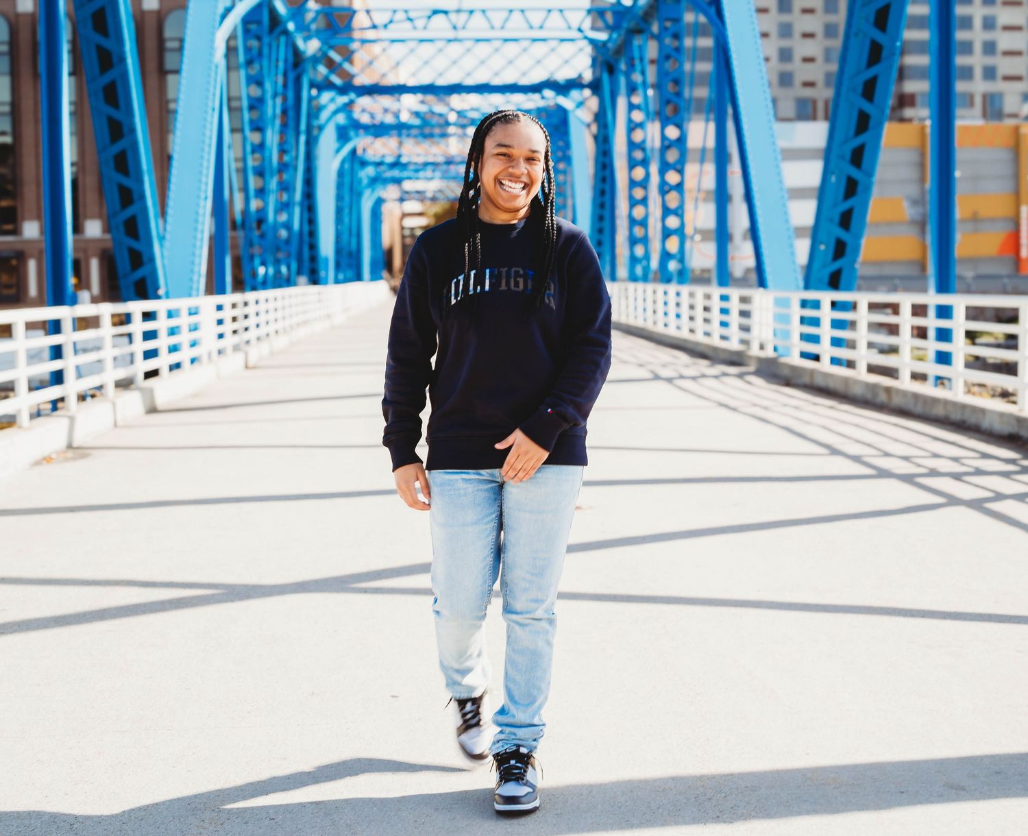 Teen walking on blue bridge in black hoodie and light jeans.
