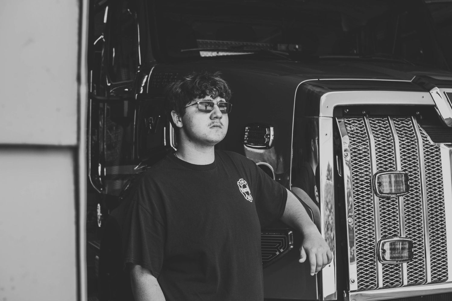 Young man in black t-shirt leaning against a large truck in a black and white portrait photo.