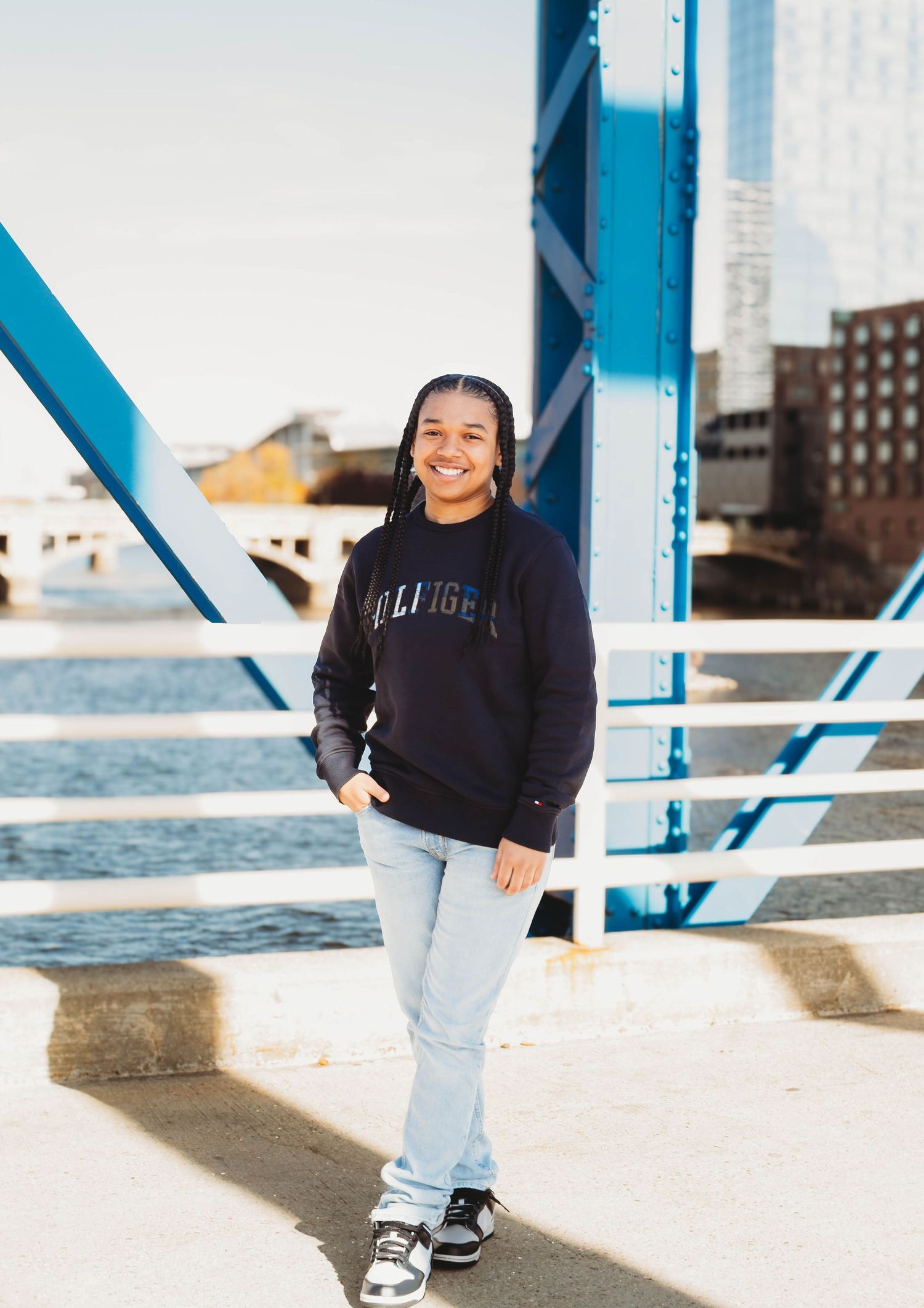 Smiling teen in navy Hilfiger hoodie posing on blue bridge.