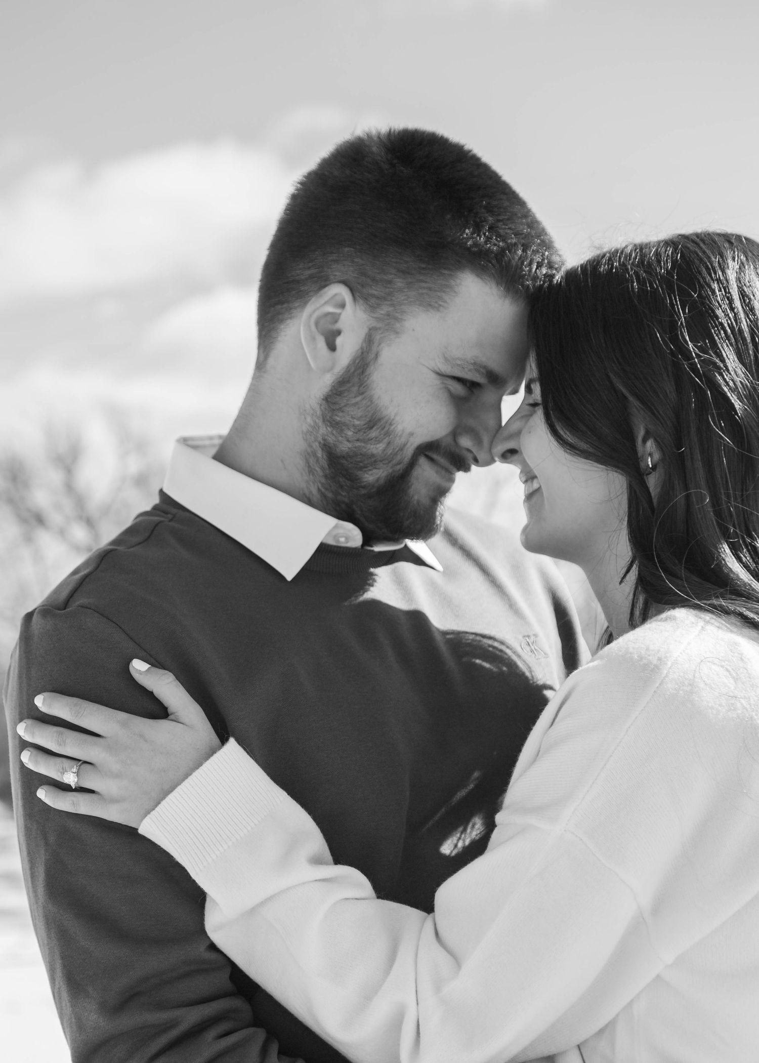 Black and white photo of a couple embracing and smiling at each other outdoors.
