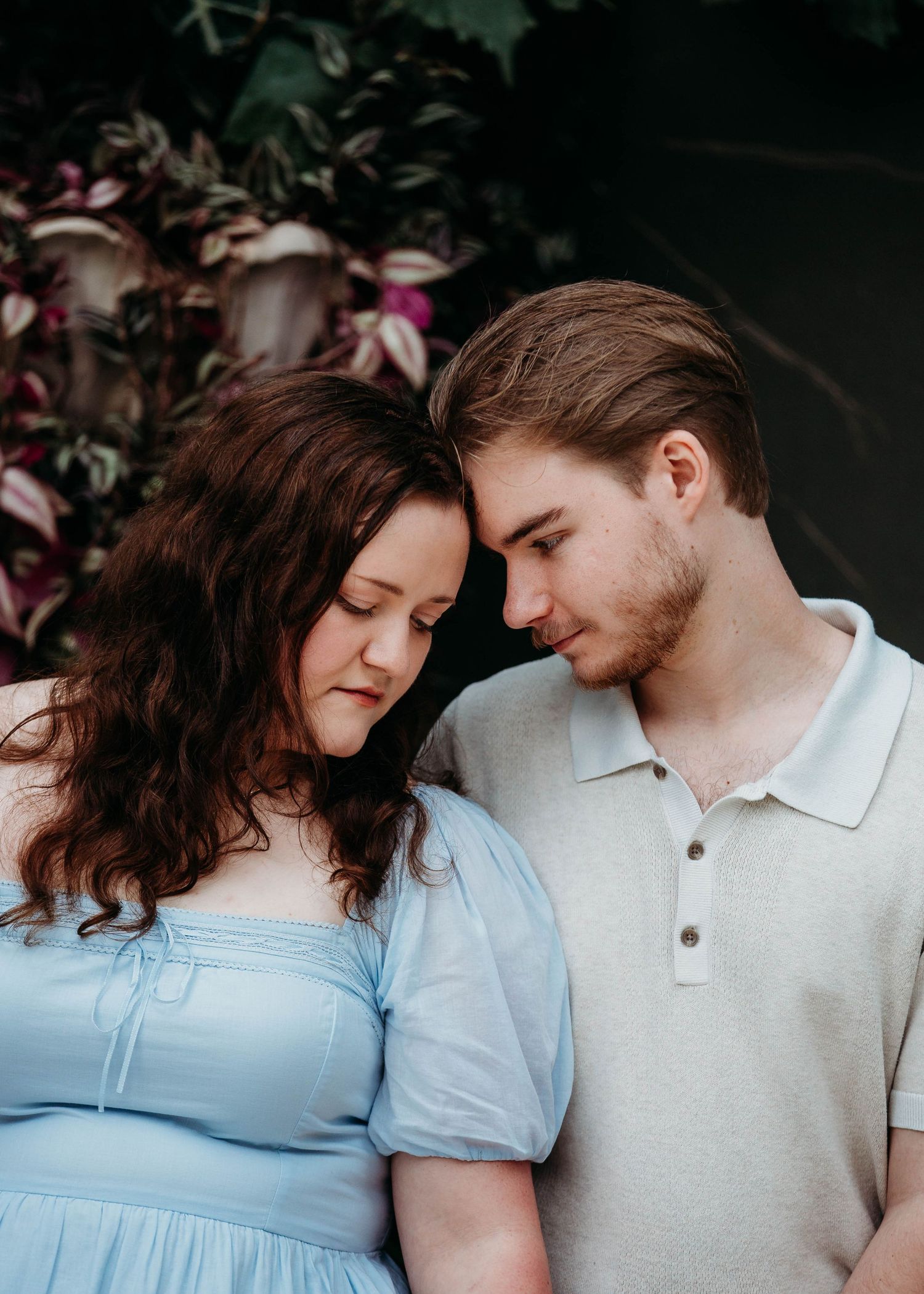 Couple leaning foreheads together tenderly in front of vibrant purple tropical foliage.