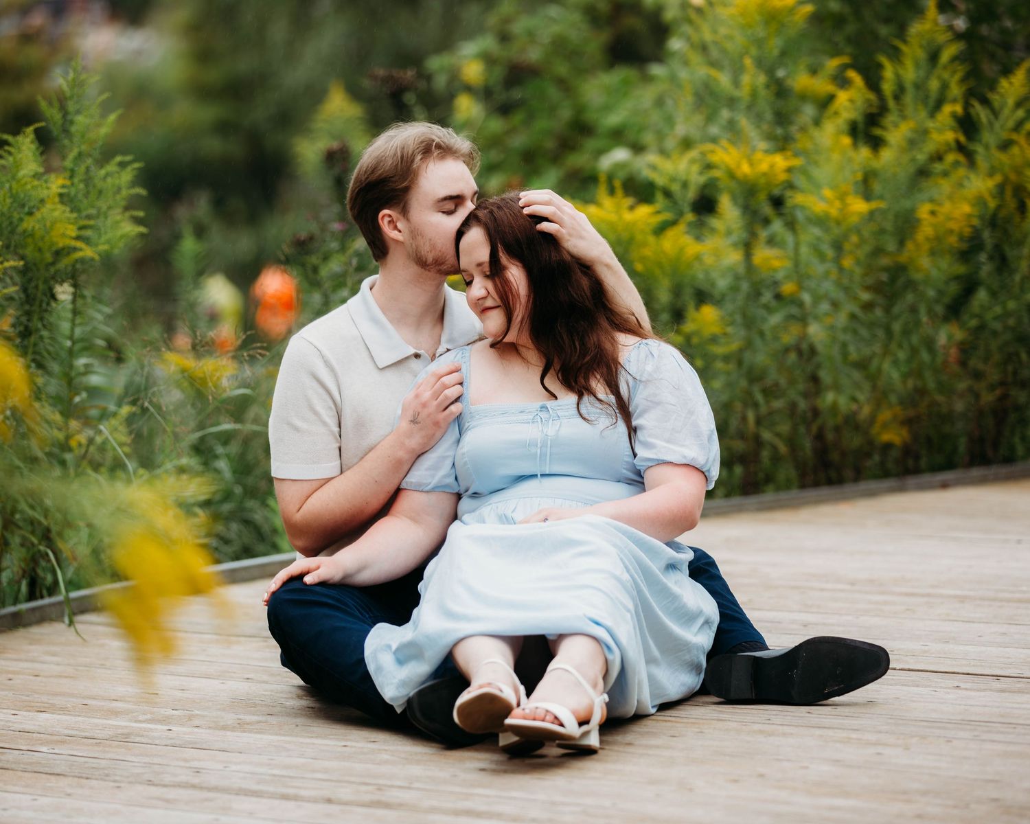 Couple sitting together on a wooden deck surrounded by vibrant yellow wildflowers in a garden.