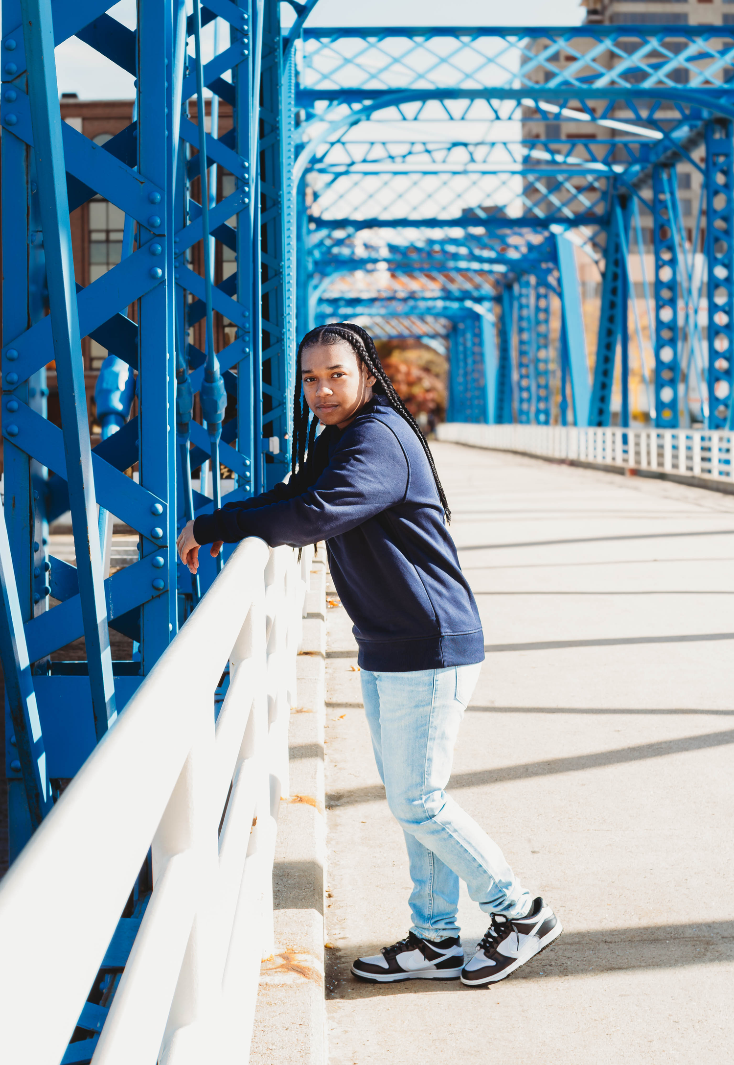 Young man leaning on blue bridge railing in navy hoodie.