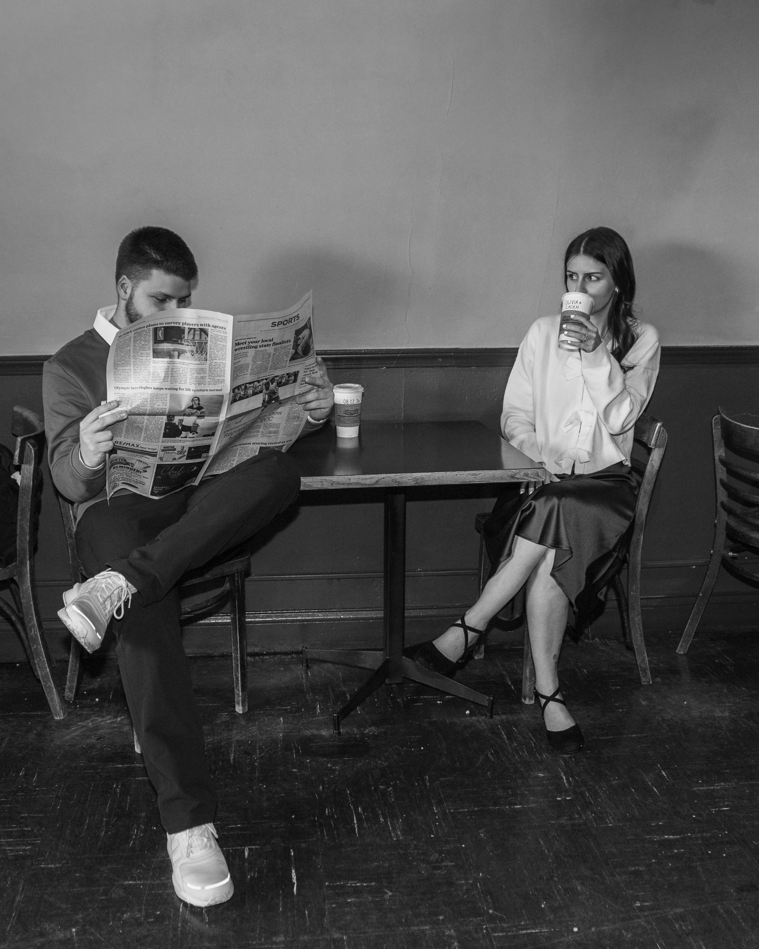 Black and white photo of a couple sitting apart at a cafe, reading and drinking coffee.