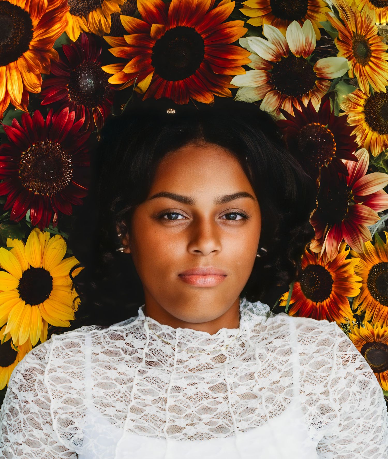 Woman lying among vibrant sunflowers wearing white lace top.