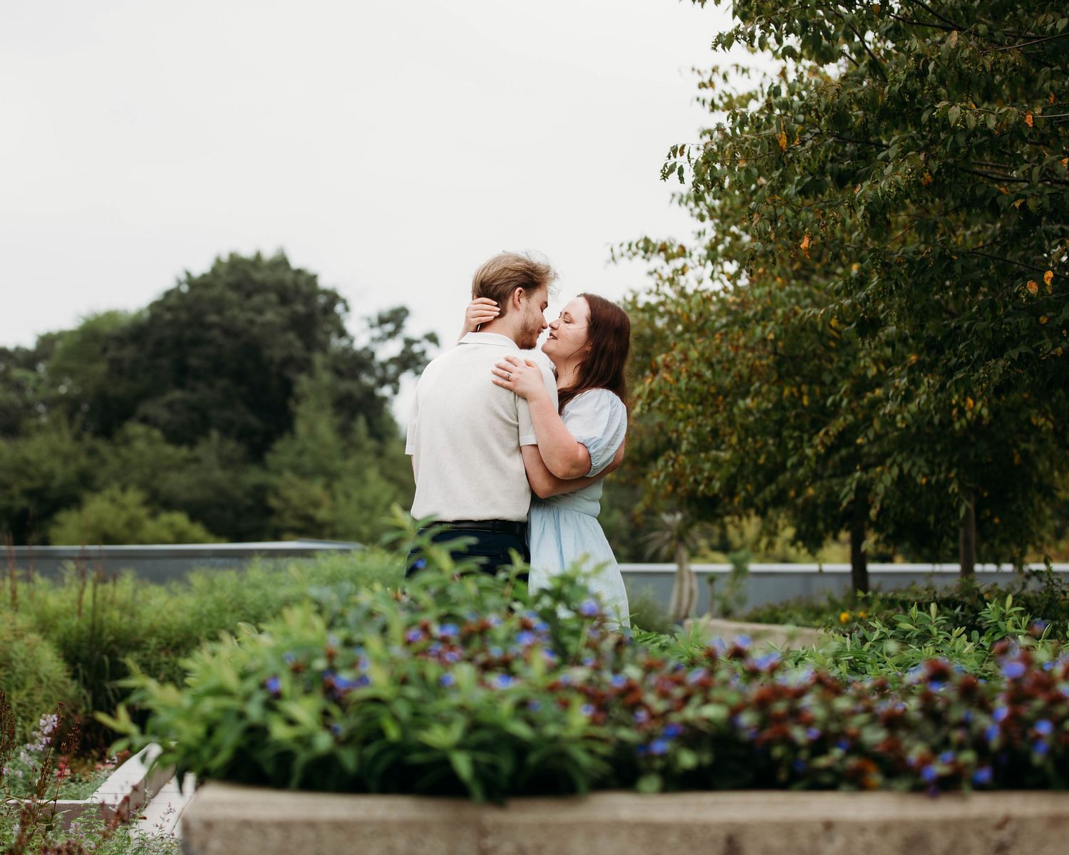 Couple embracing and almost kissing in a lush garden with colorful flowers in the foreground.