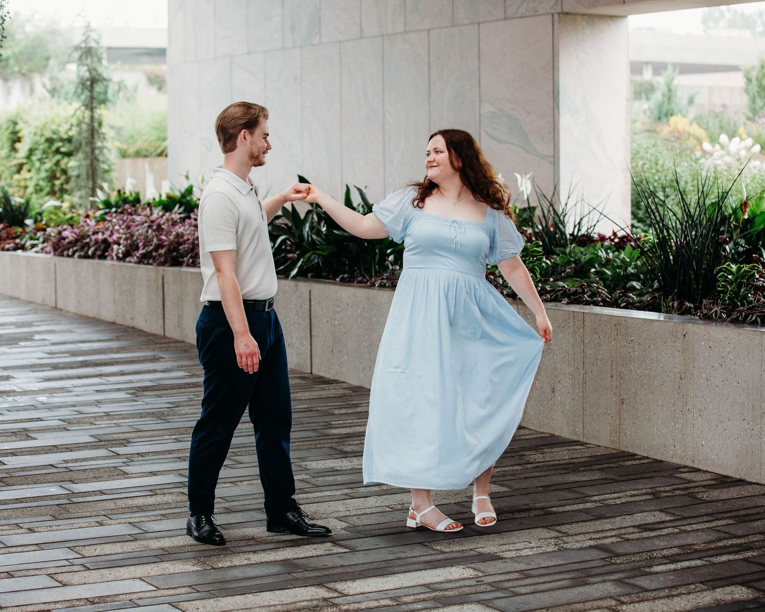 Couple dancing playfully on a stone patio with manicured hedges in the background.