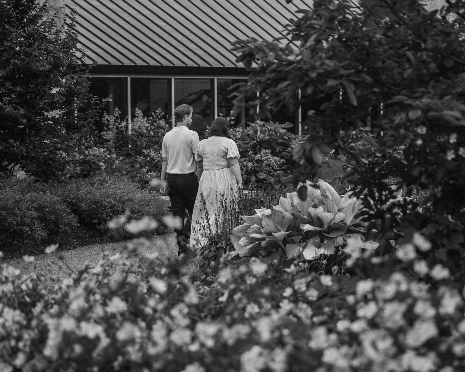 Black and white photo of a couple walking hand in hand through a blooming garden path.