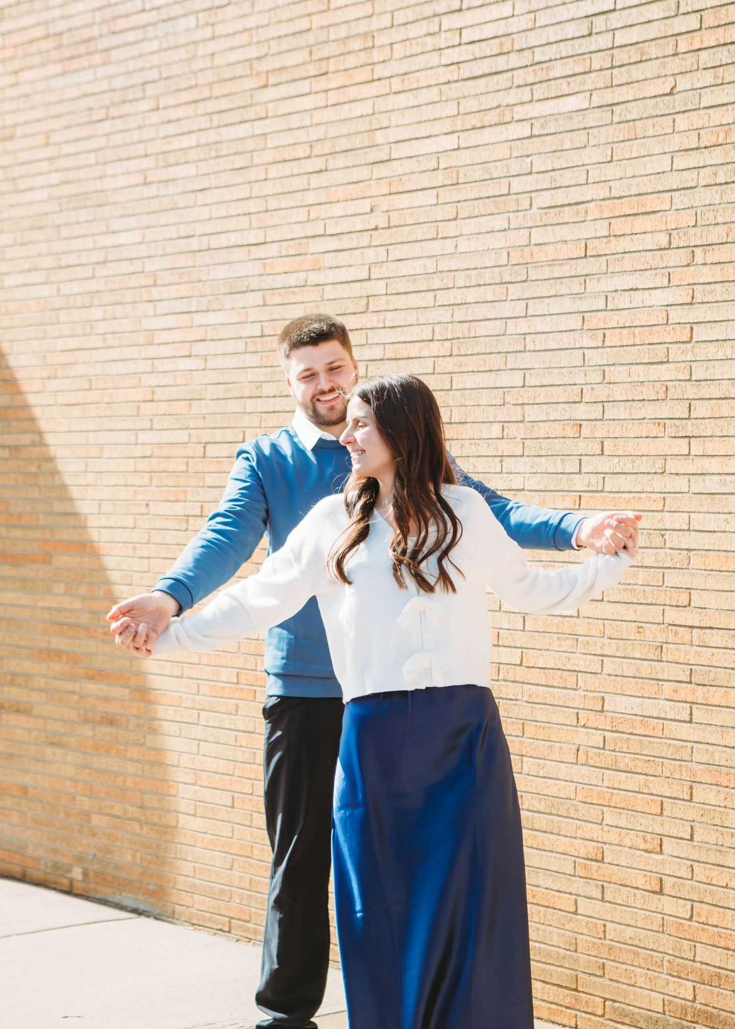 Happy couple dancing together outdoors against a warm brick wall in coordinating blue outfits.
