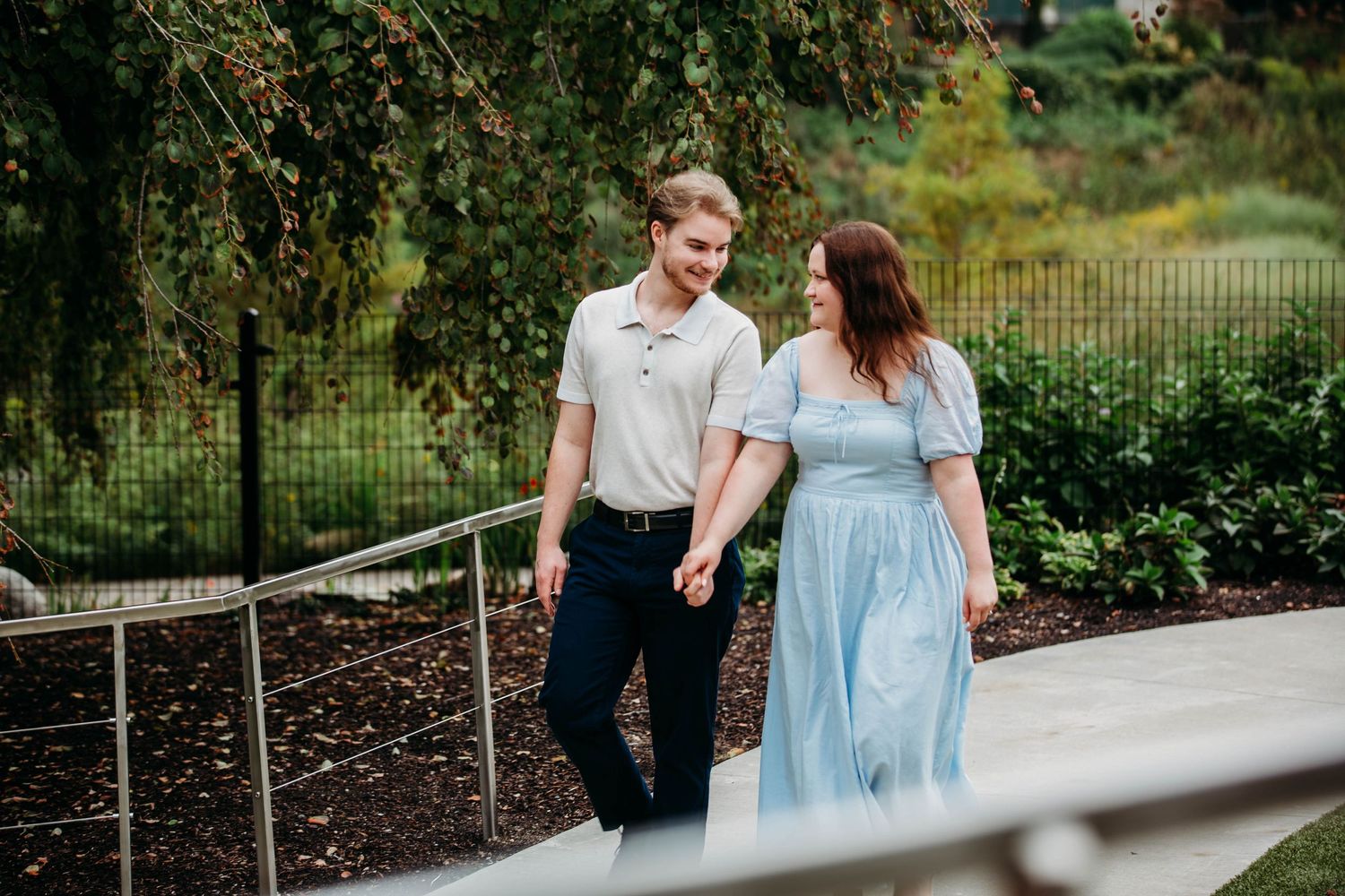 Happy couple holding hands and walking along a garden path with lush greenery.
